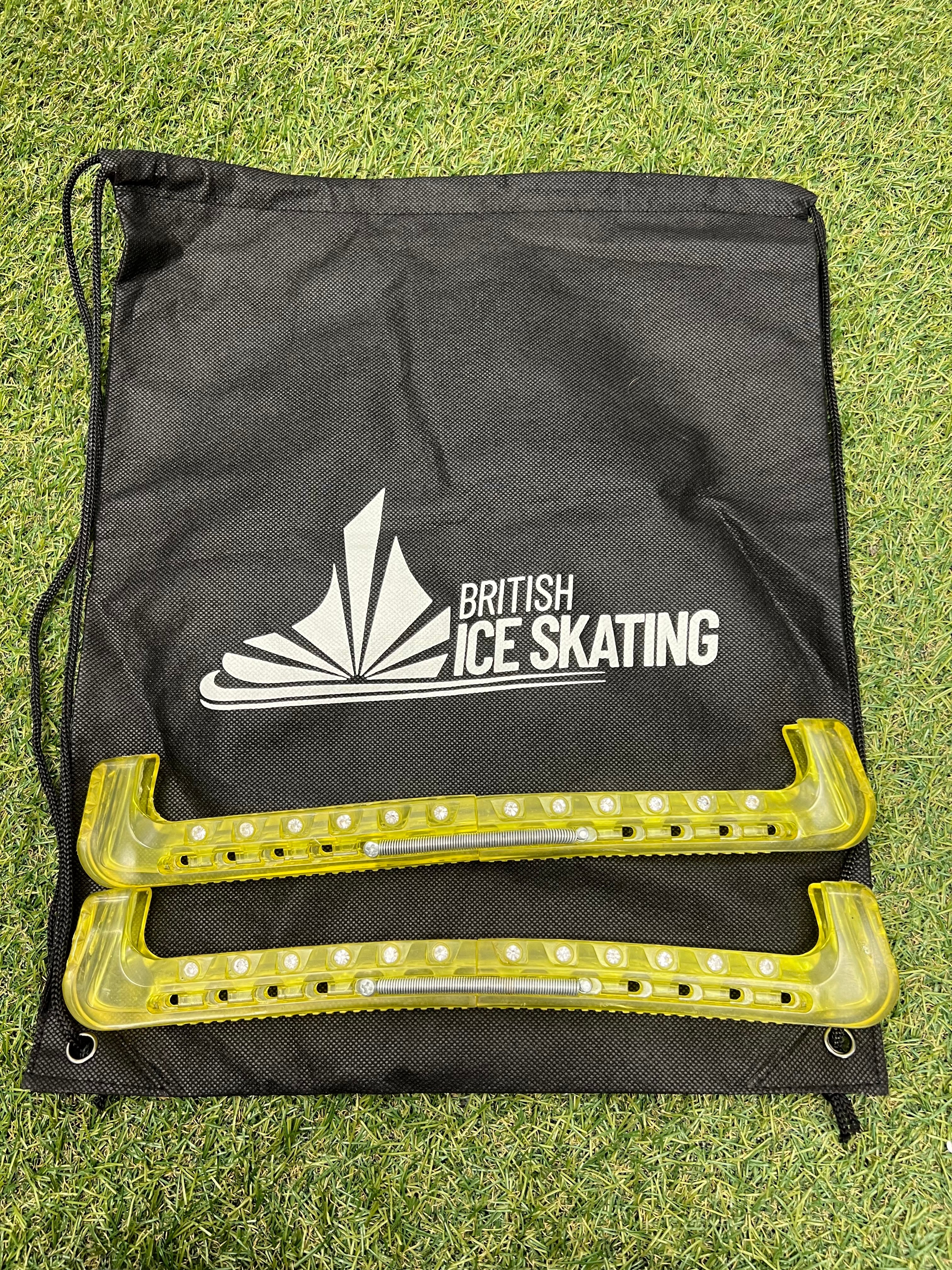 British Ice Skating branded black drawstring bag with yellow protective blade guards on grass