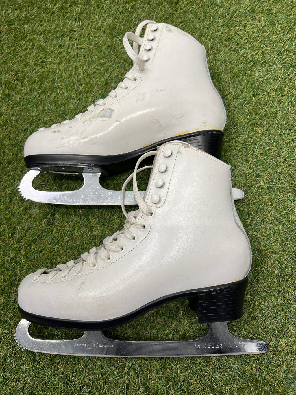 Side view of white figure skates showing black heel and sharp stainless steel blades