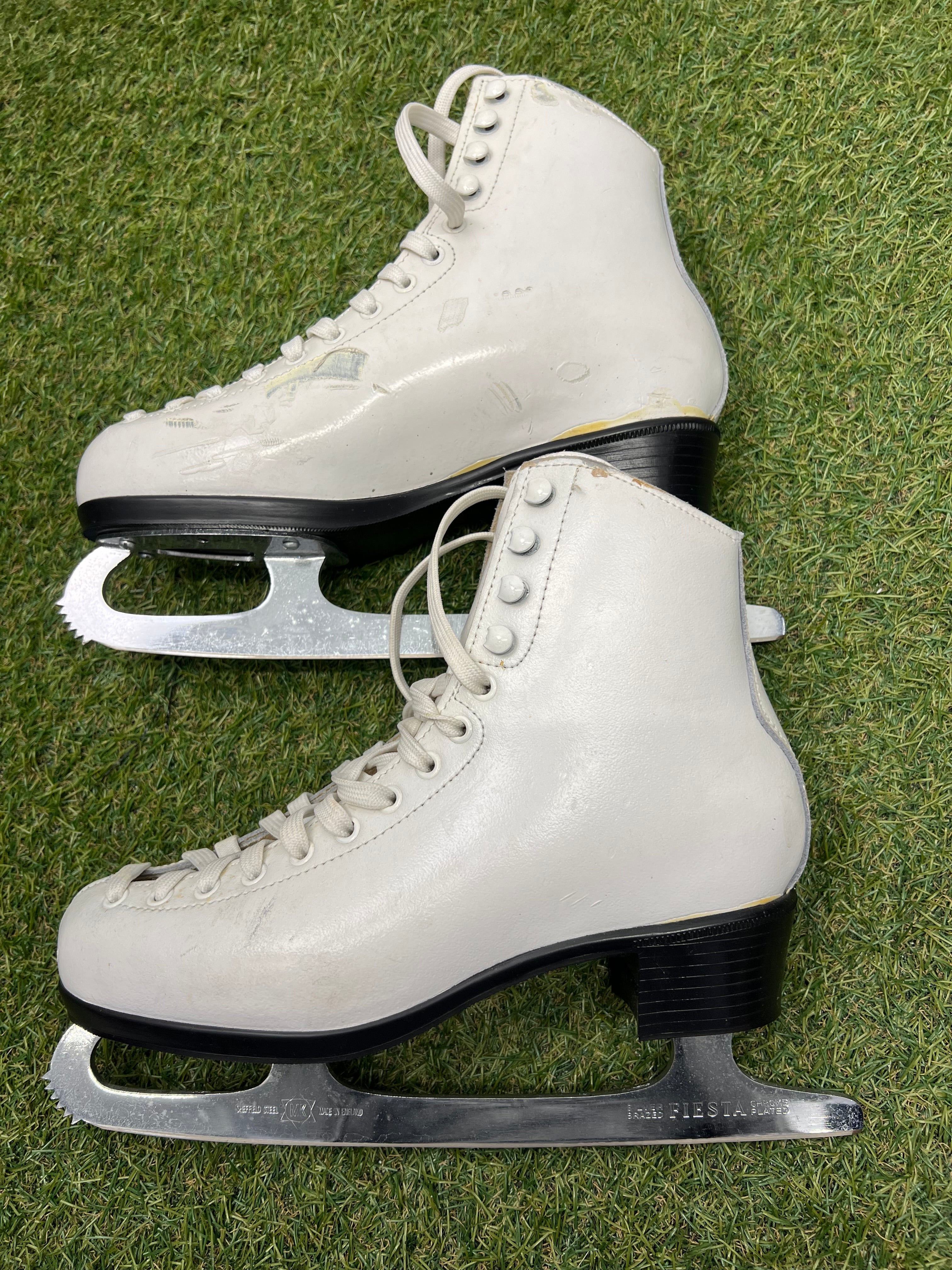Side view of white figure skates showing black heel and sharp stainless steel blades