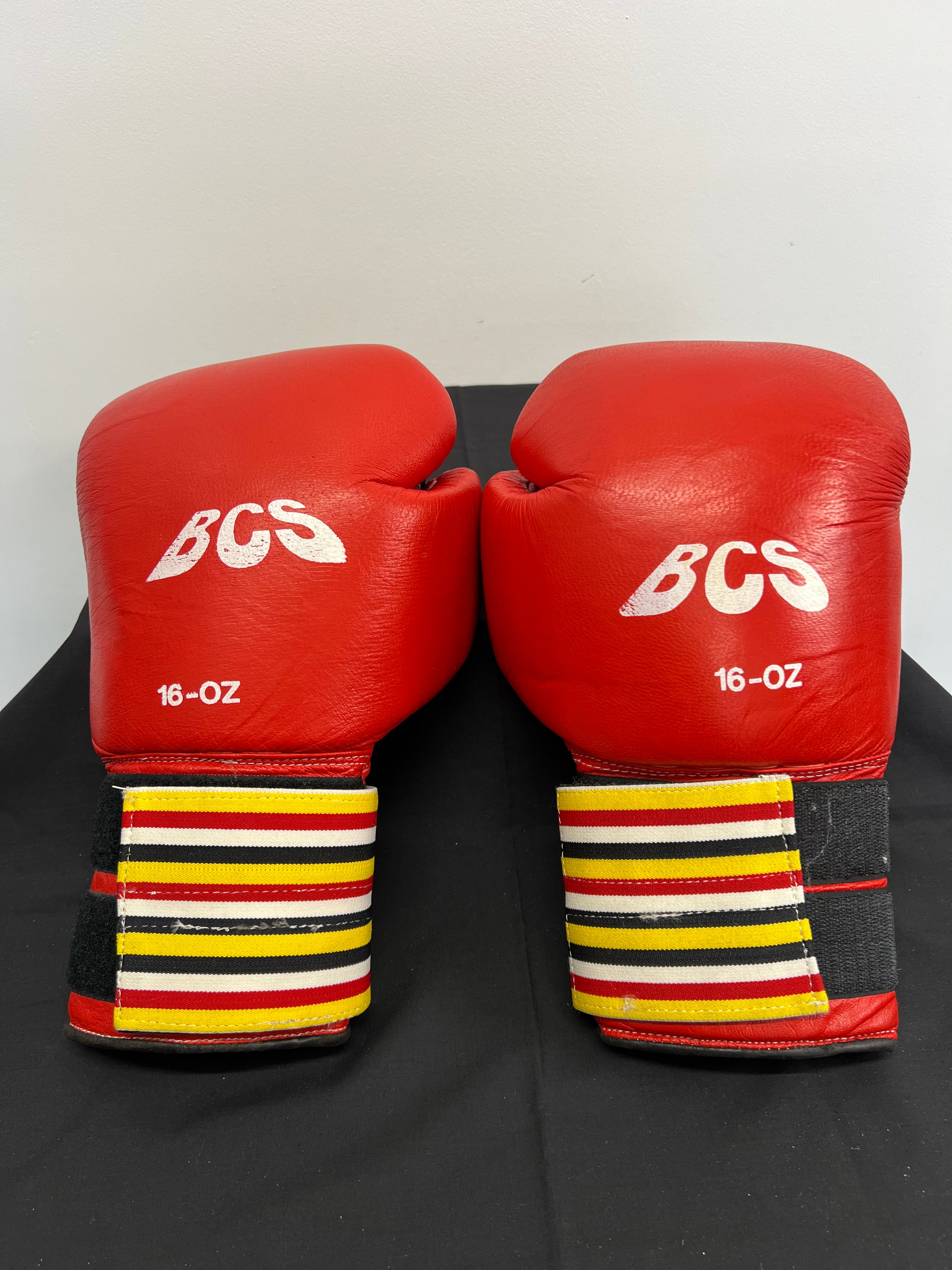 Pair of red BCS 16oz boxing gloves with striped wrist straps front view