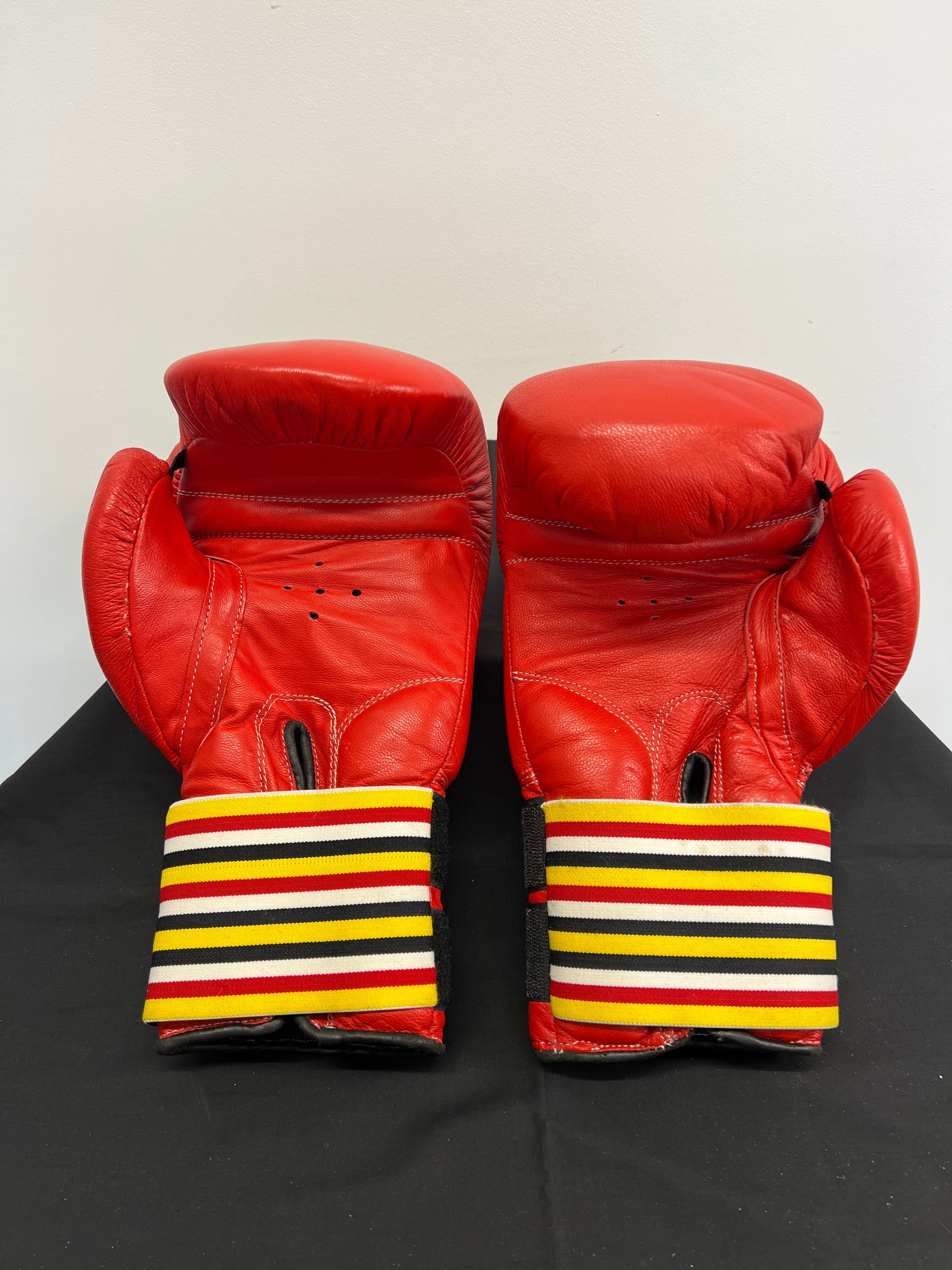 Red BCS 16oz boxing gloves showing palm side and ventilation holes with colourful striped wrist straps
