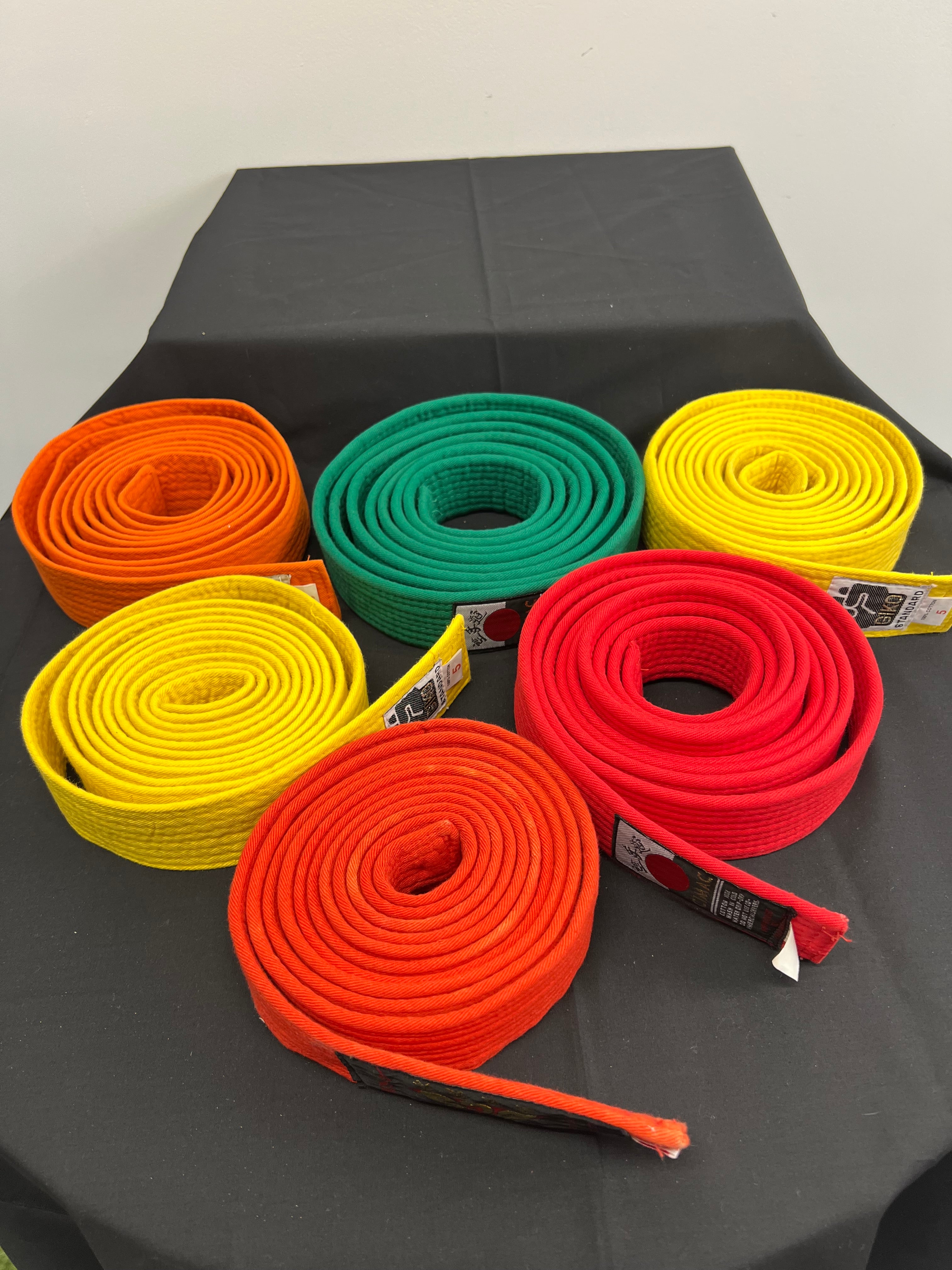 Set of six rolled martial arts belts in orange, green, yellow, and red on black surface