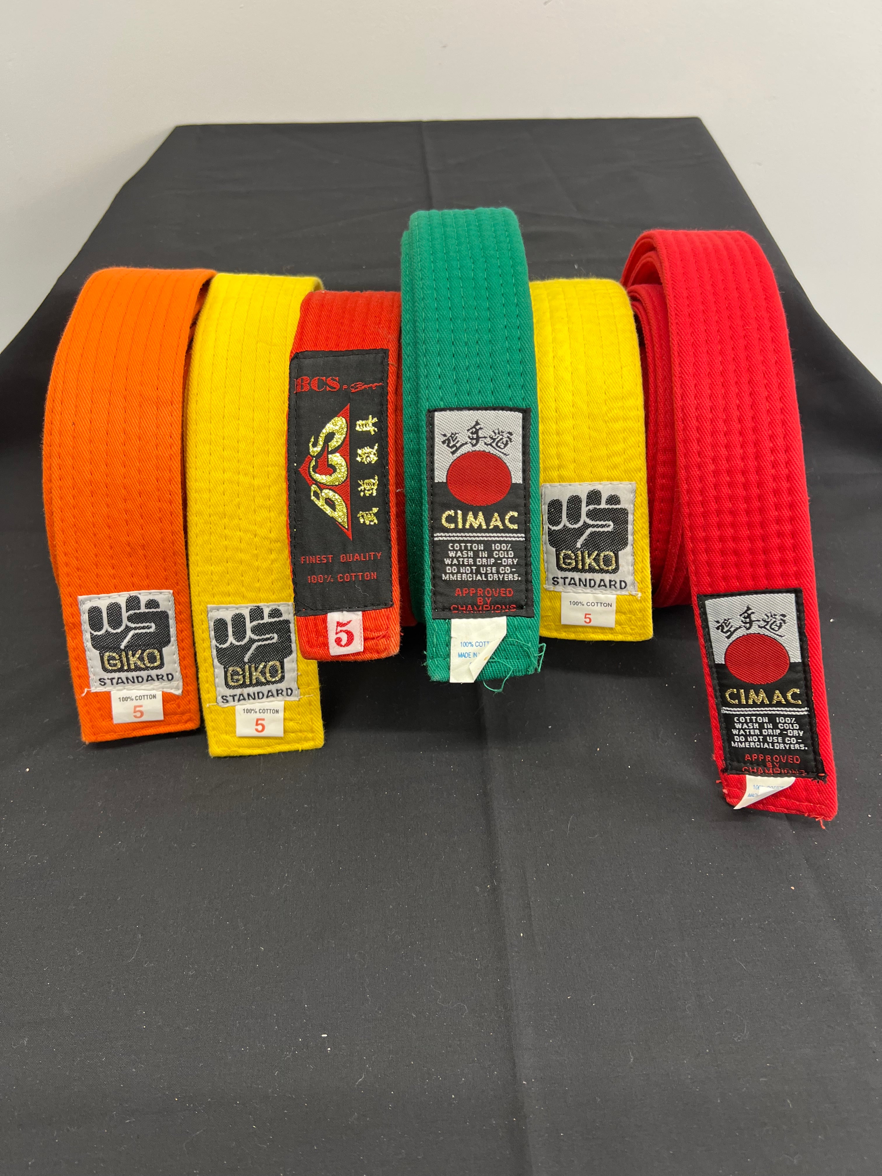 Close-up of martial arts belts showing brand tags GIKO, BCS, and CIMAC with size 5 labels