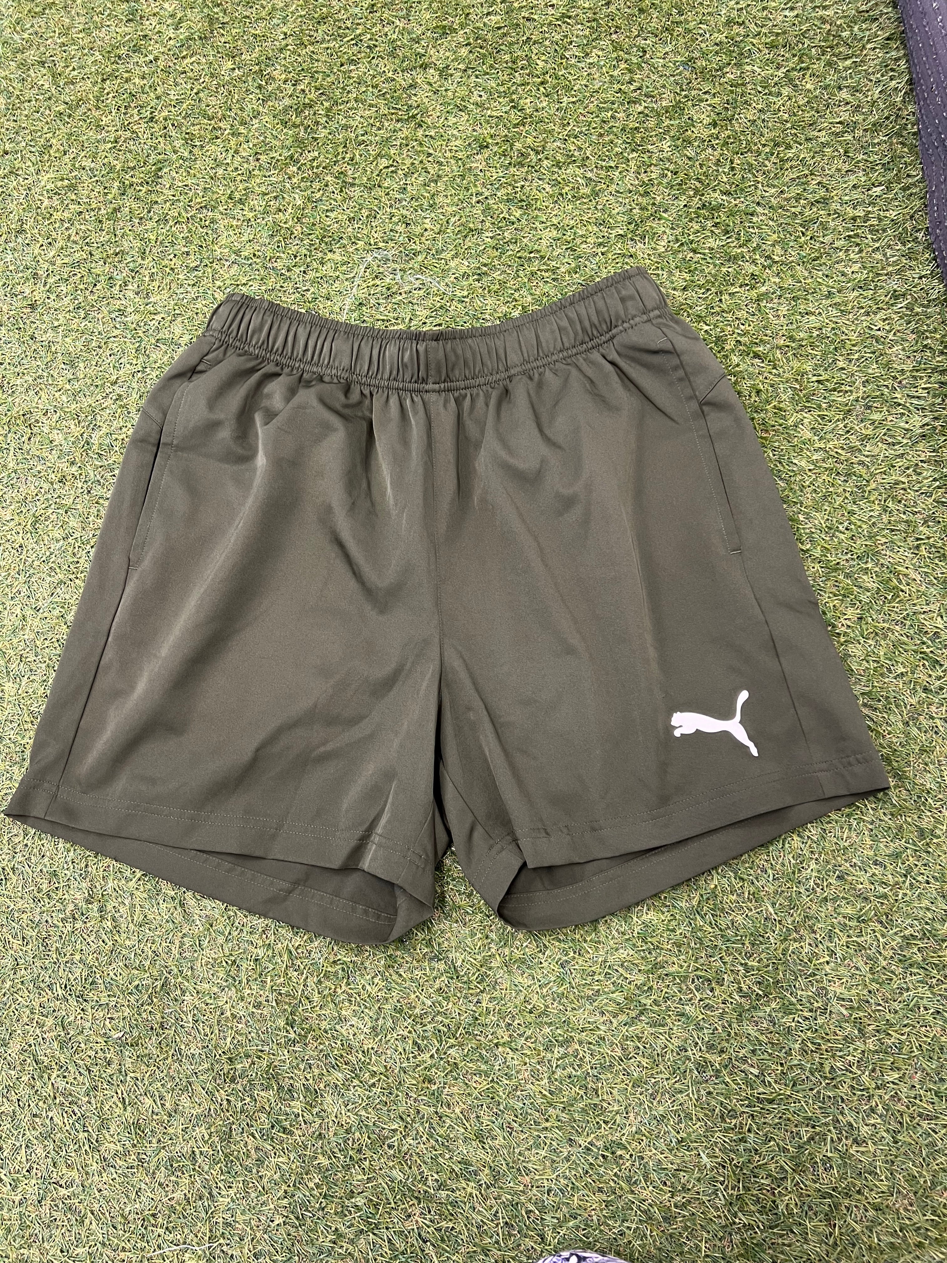 Front view of men's olive green Puma sports shorts on grass