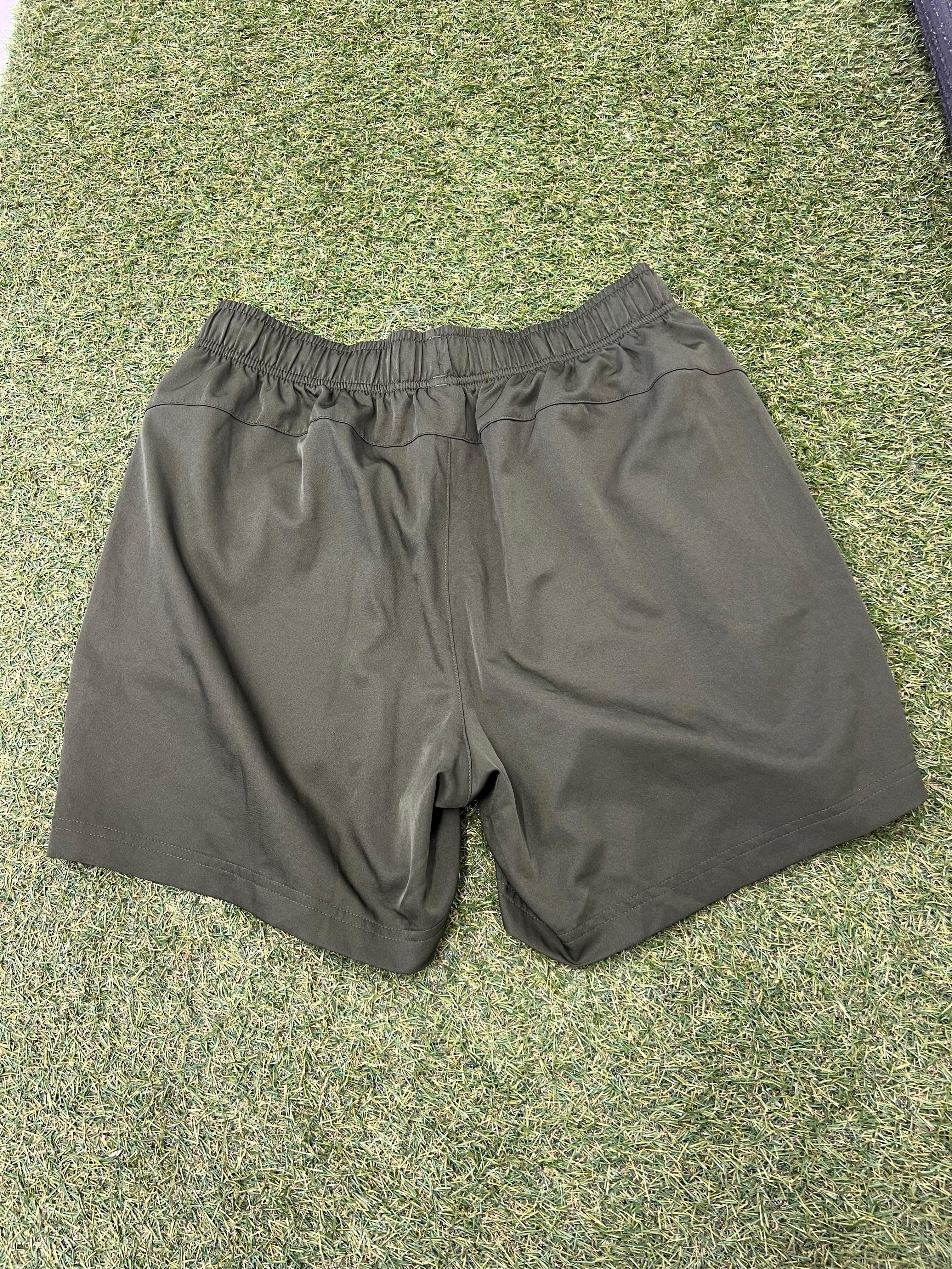Back view of men's olive green Puma sports shorts on grass