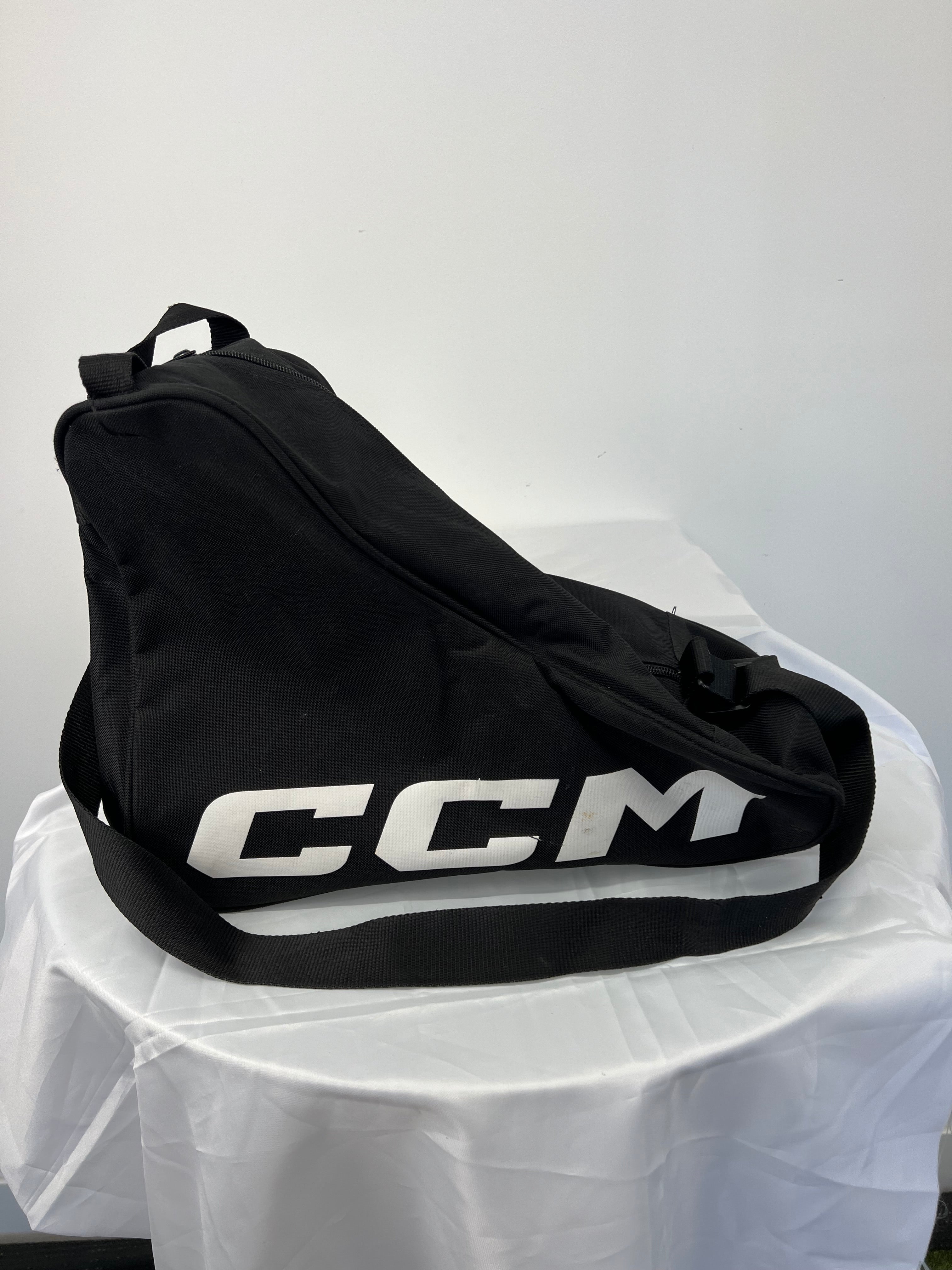 Black CCM ice skate bag side view with shoulder strap on white surface