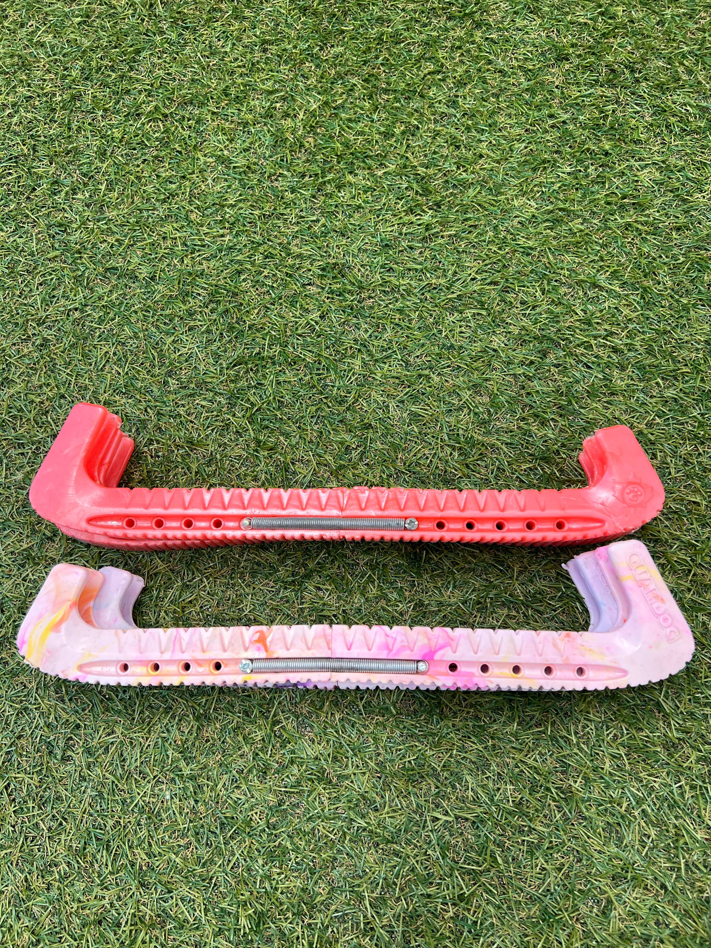 Pack of two ice skate blade guards on grass, one red and one pastel multicolour