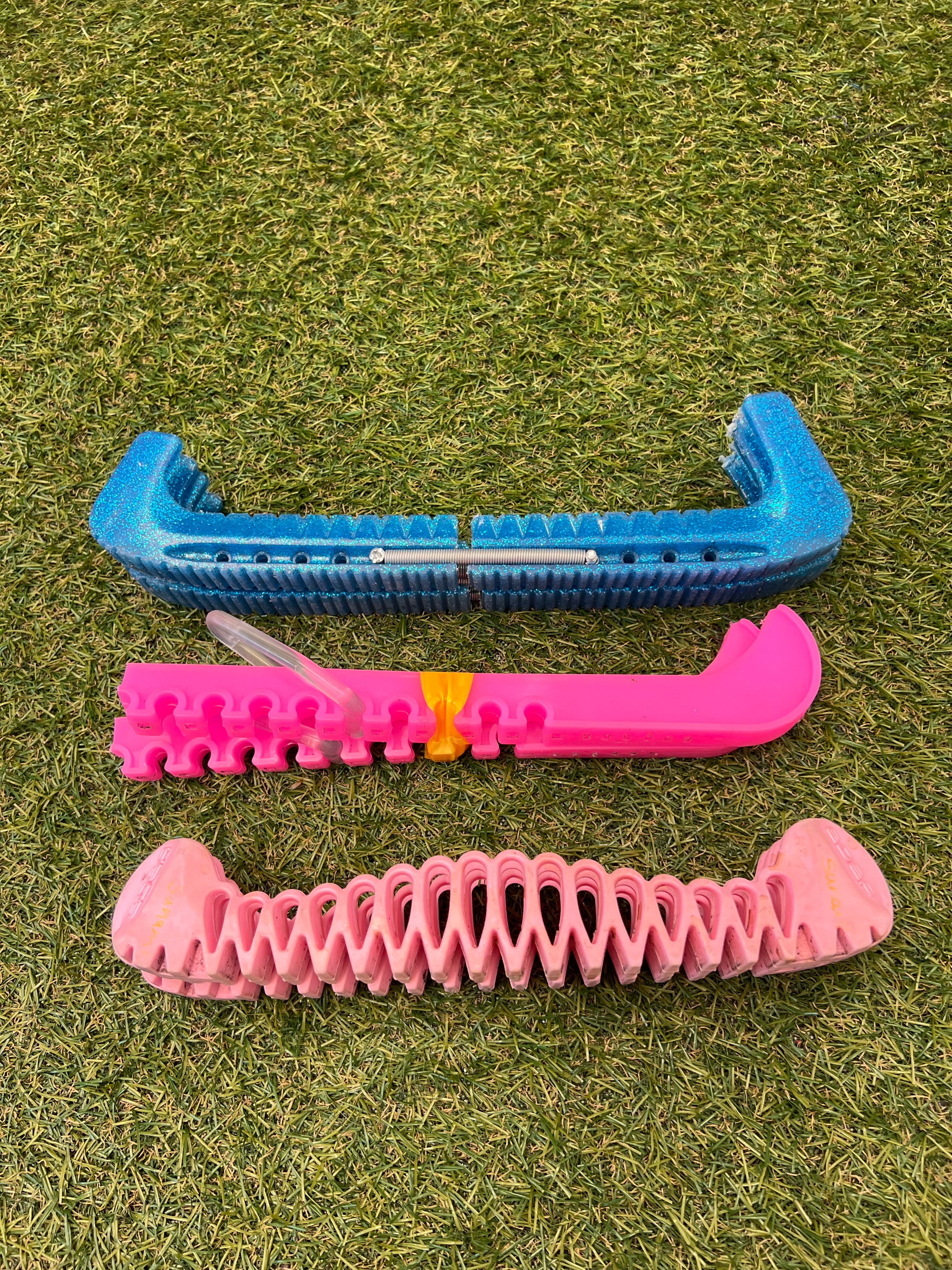 Three adjustable ice skate blade guards in blue and pink on grass