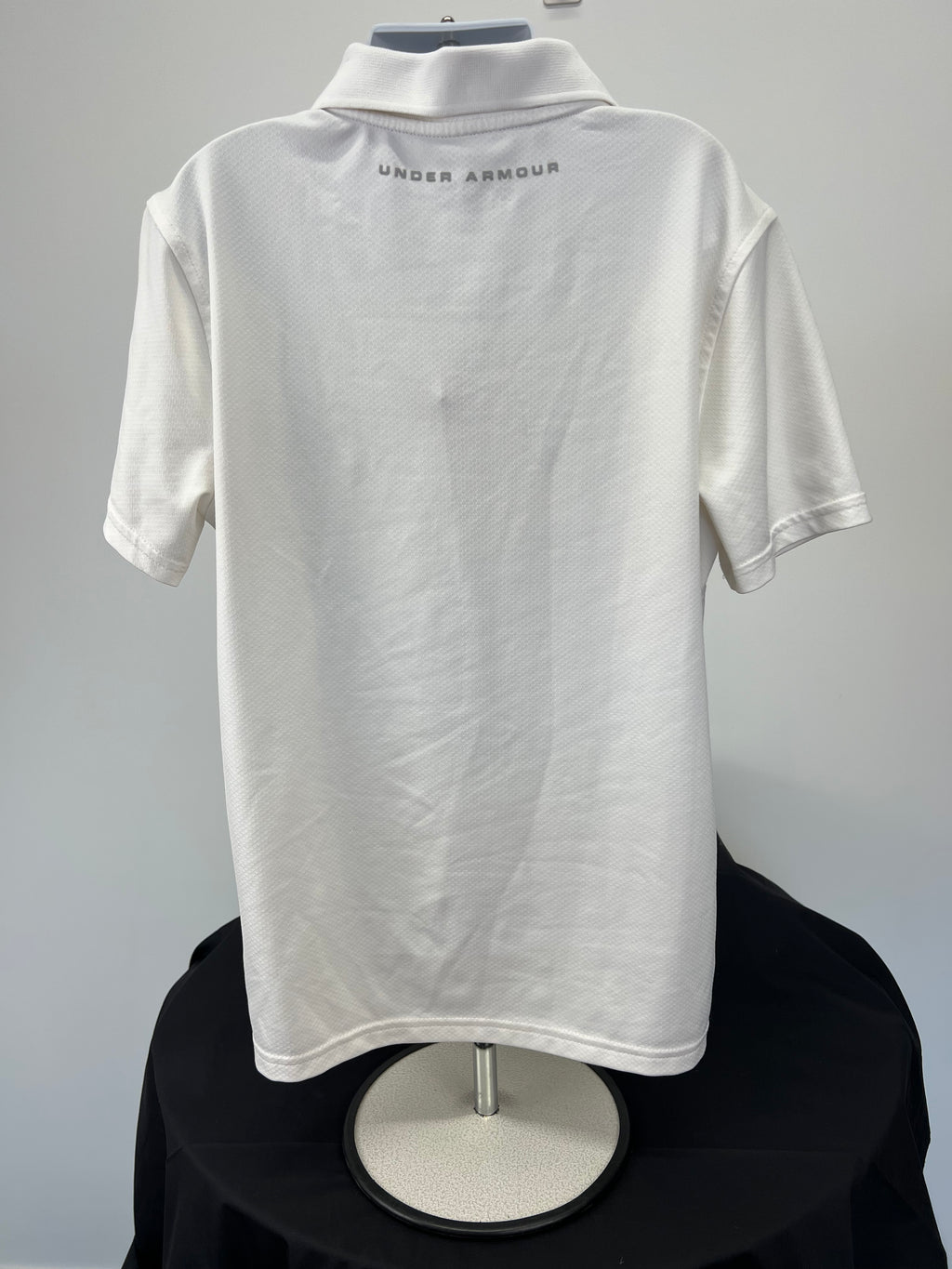 Back view of white Under Armour youth polo shirt with branded text