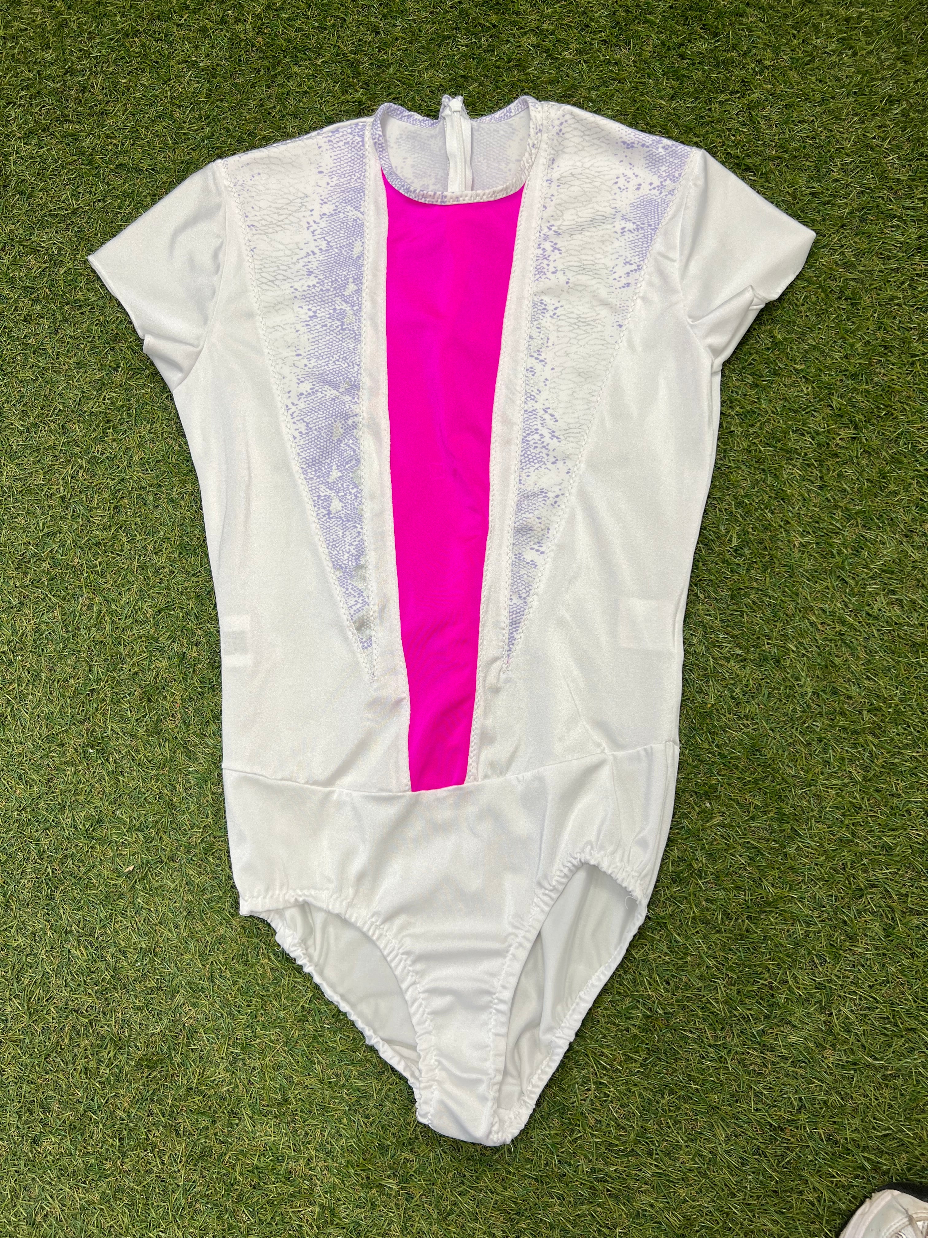 Front view of white short sleeve figure skating leotard with bright pink centre panel and lilac snake-print accents on grass background