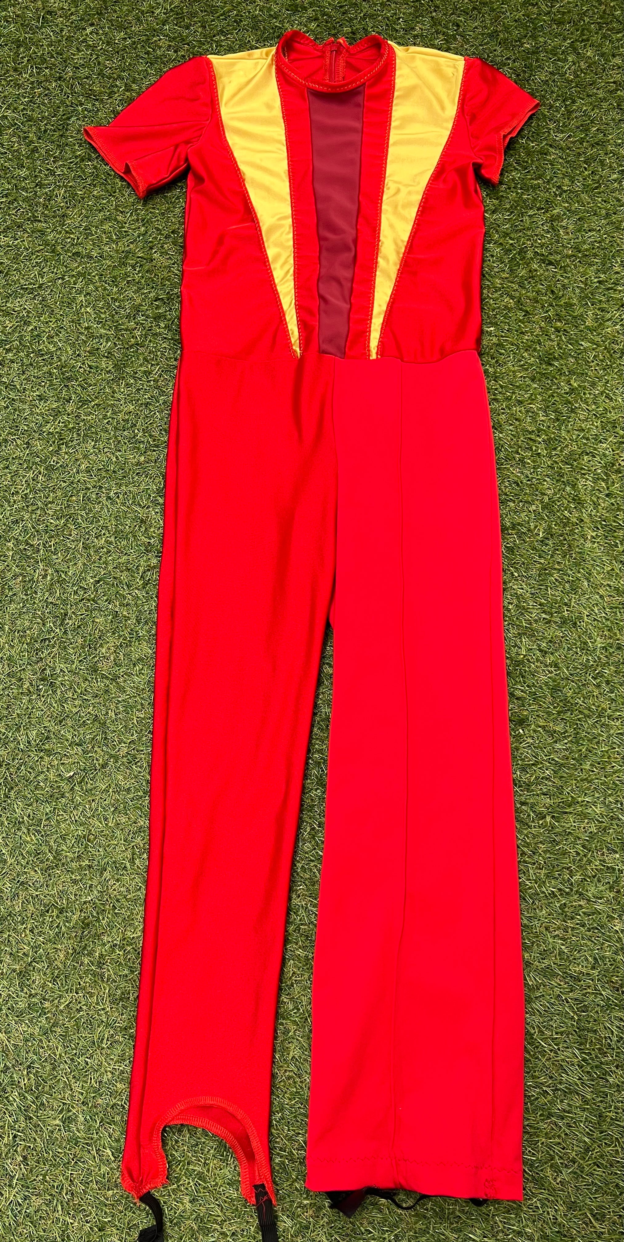 Front view of red kids ice skating jumpsuit with yellow and dark red panel design and short sleeves