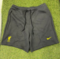 Front view of black Nike men's shorts with yellow Liverpool FC logo and Nike swoosh on grass background