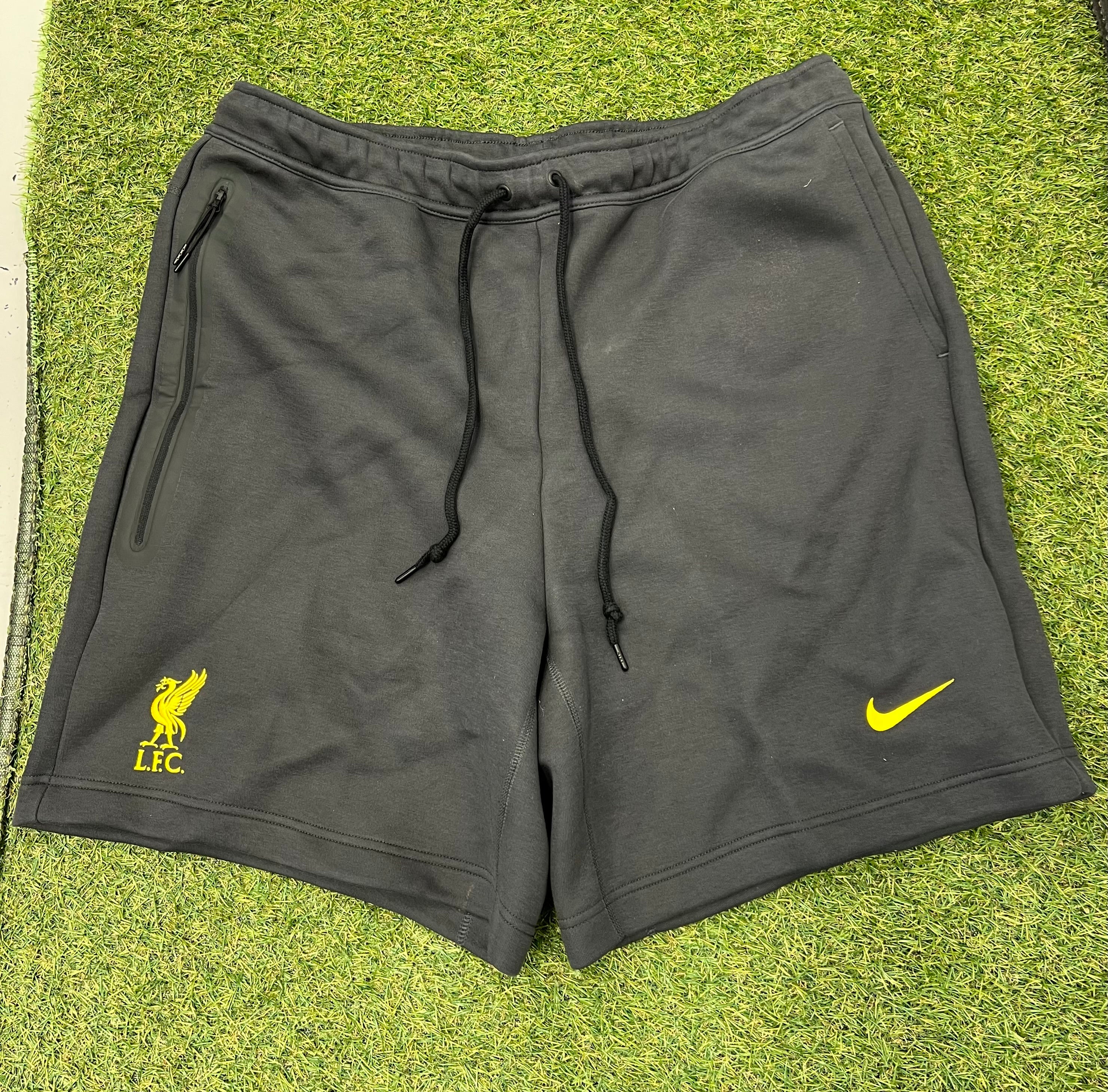 Front view of black Nike men's shorts with yellow Liverpool FC logo and Nike swoosh on grass background