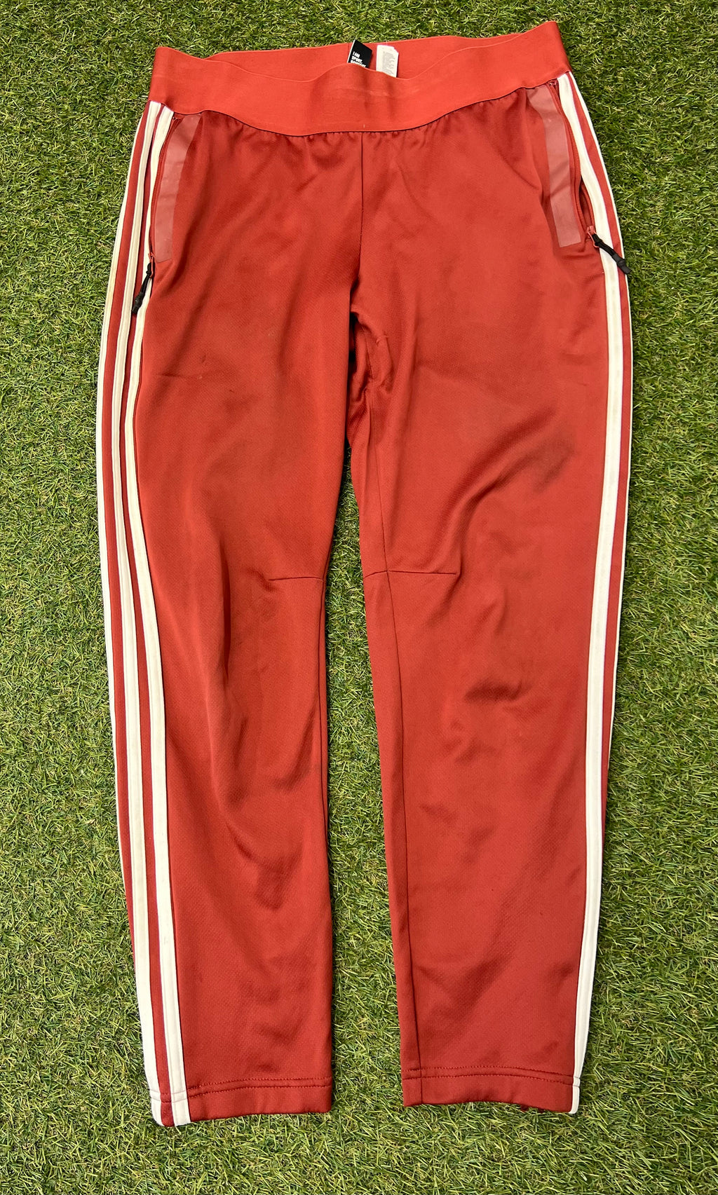 Front view of red Adidas women's tracksuit bottoms with white side stripes and zippered pockets