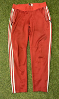 Front view of red Adidas women's tracksuit bottoms with white side stripes and zippered pockets