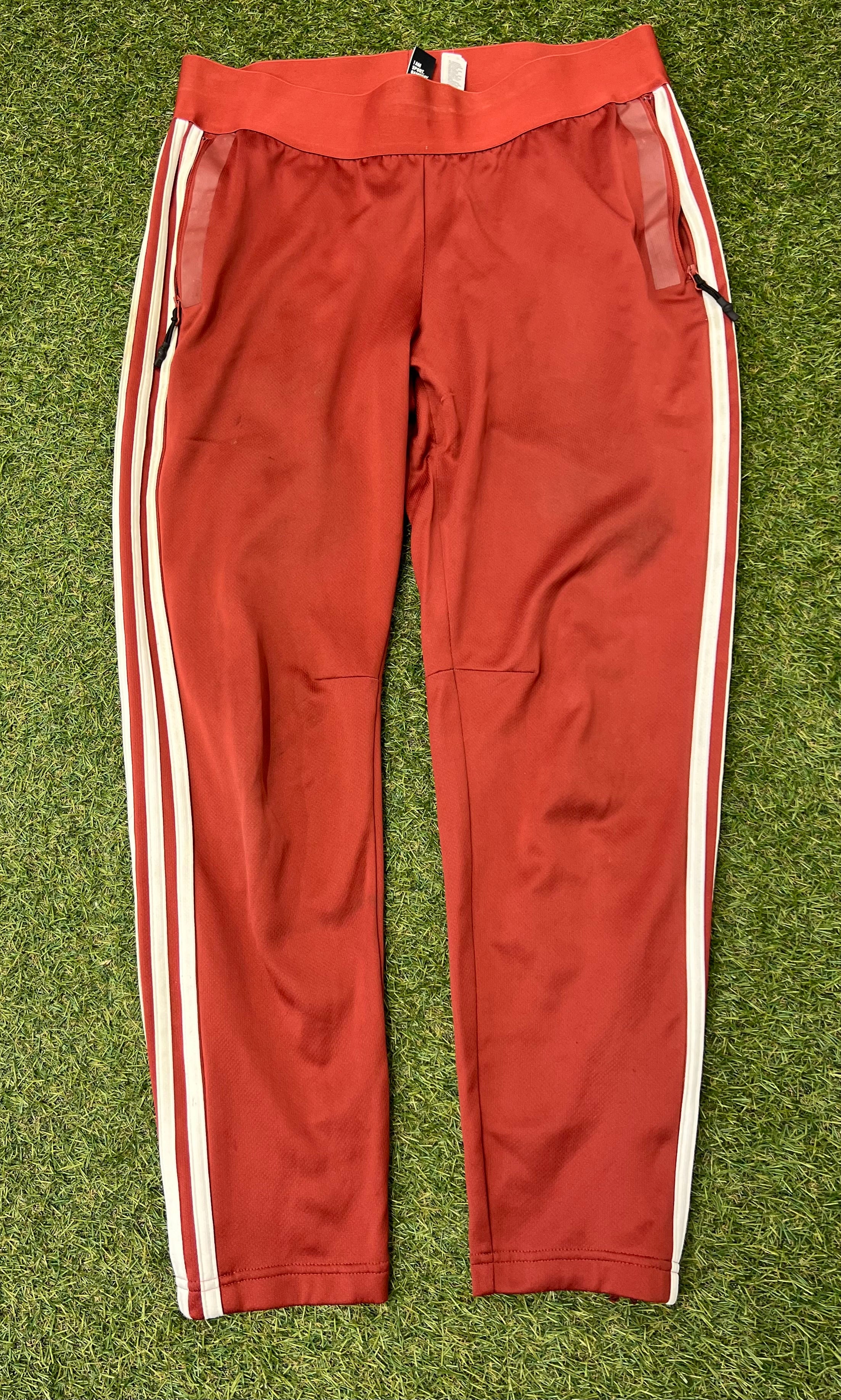 Front view of red Adidas women's tracksuit bottoms with white side stripes and zippered pockets