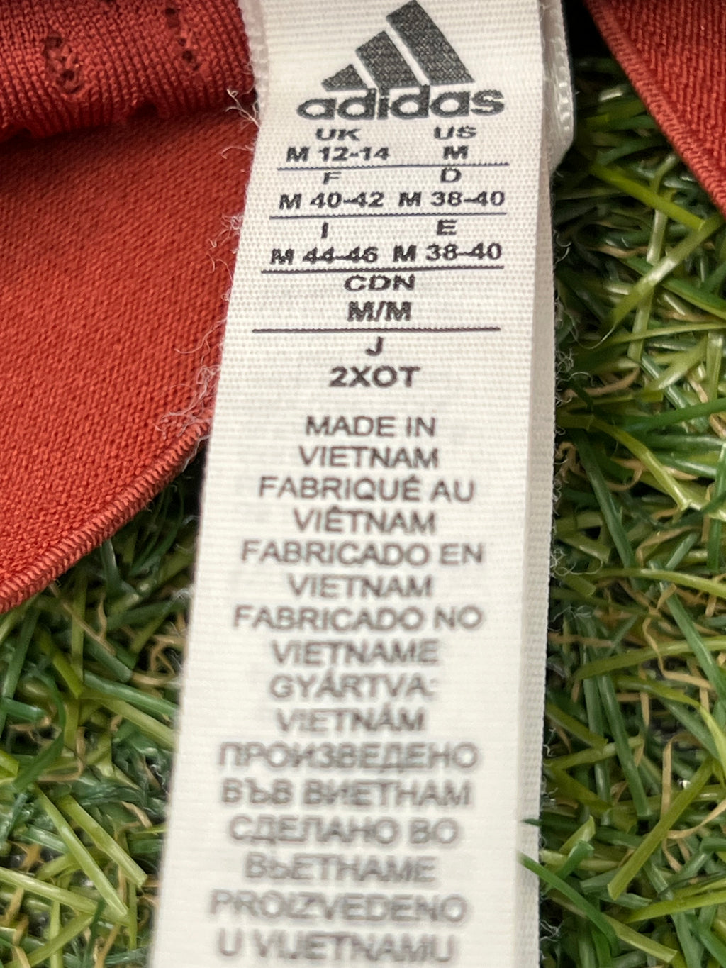 Close-up of Adidas label on red tracksuit bottoms showing size and manufacturing details