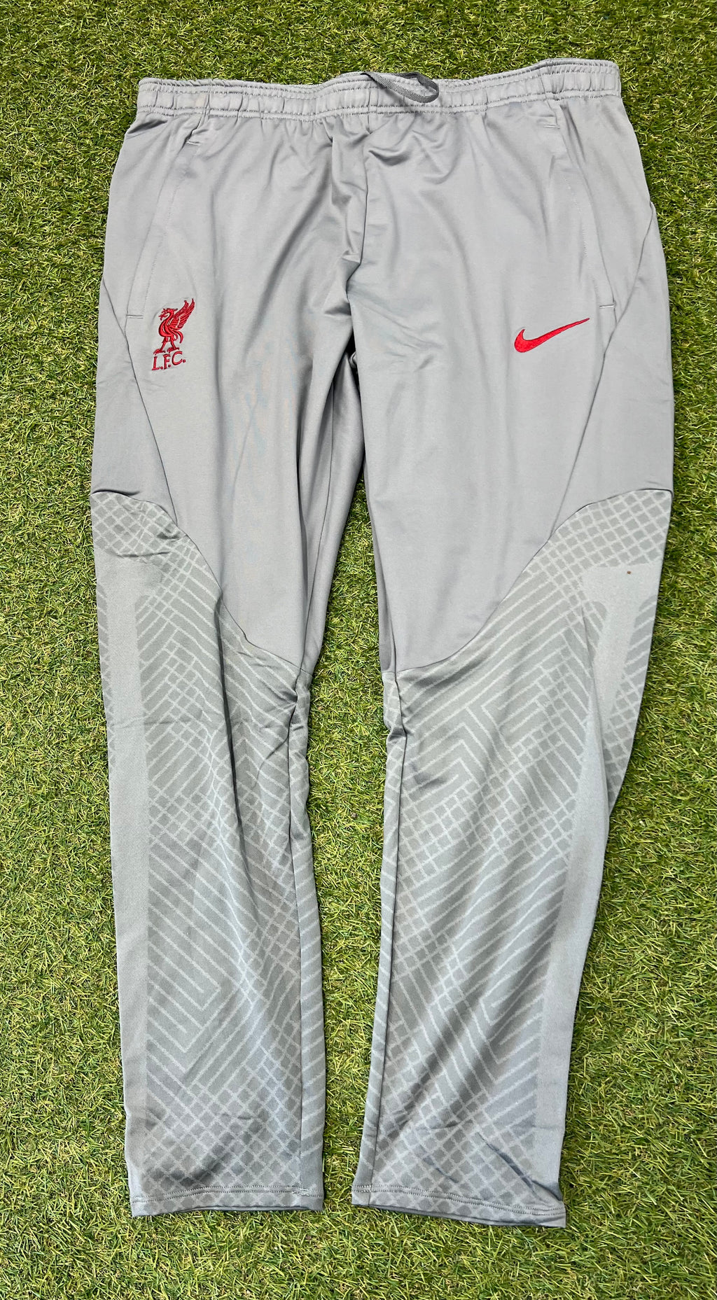 Front view of grey Nike Liverpool FC slim fit tracksuit bottoms laid flat on grass