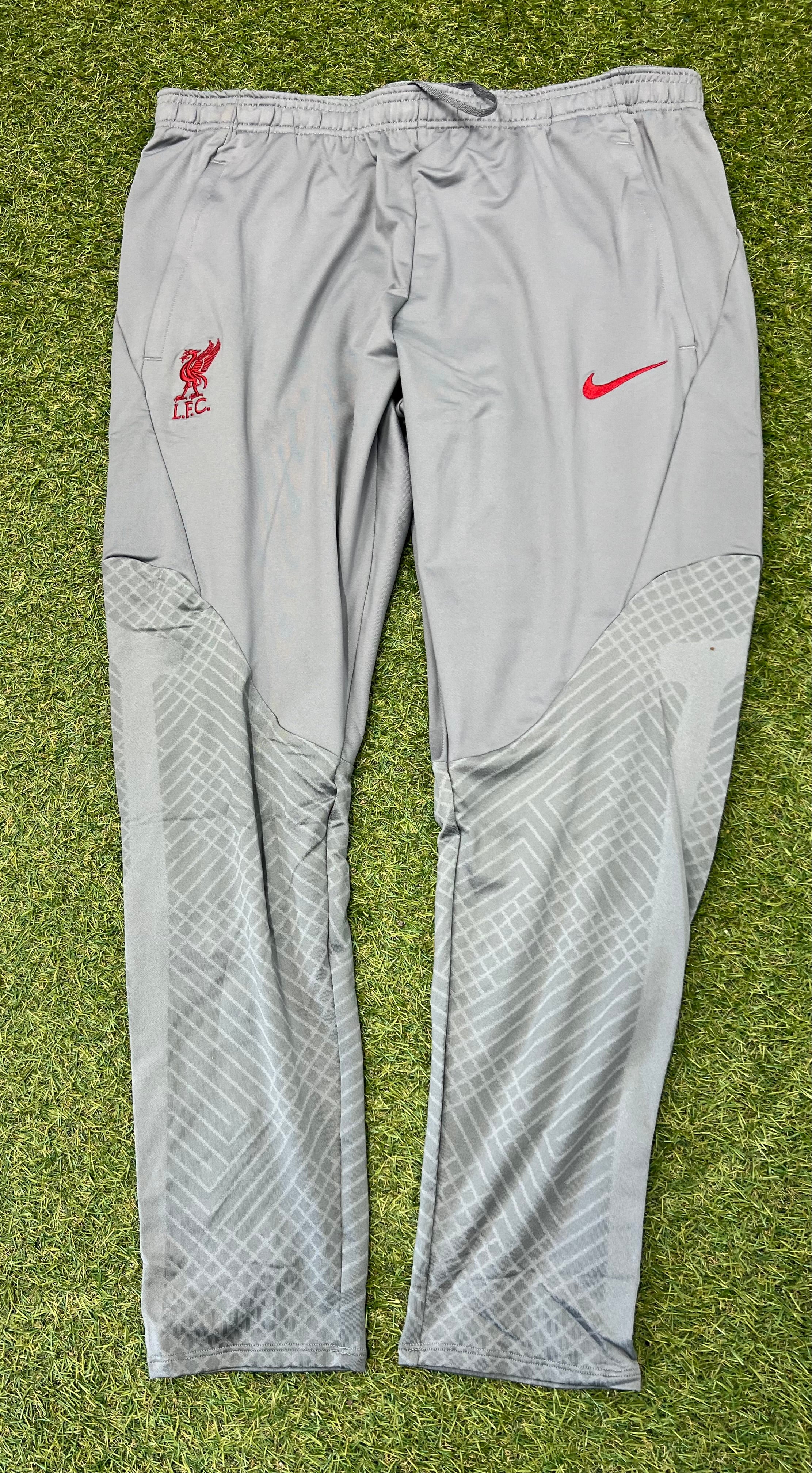 Front view of grey Nike Liverpool FC slim fit tracksuit bottoms laid flat on grass