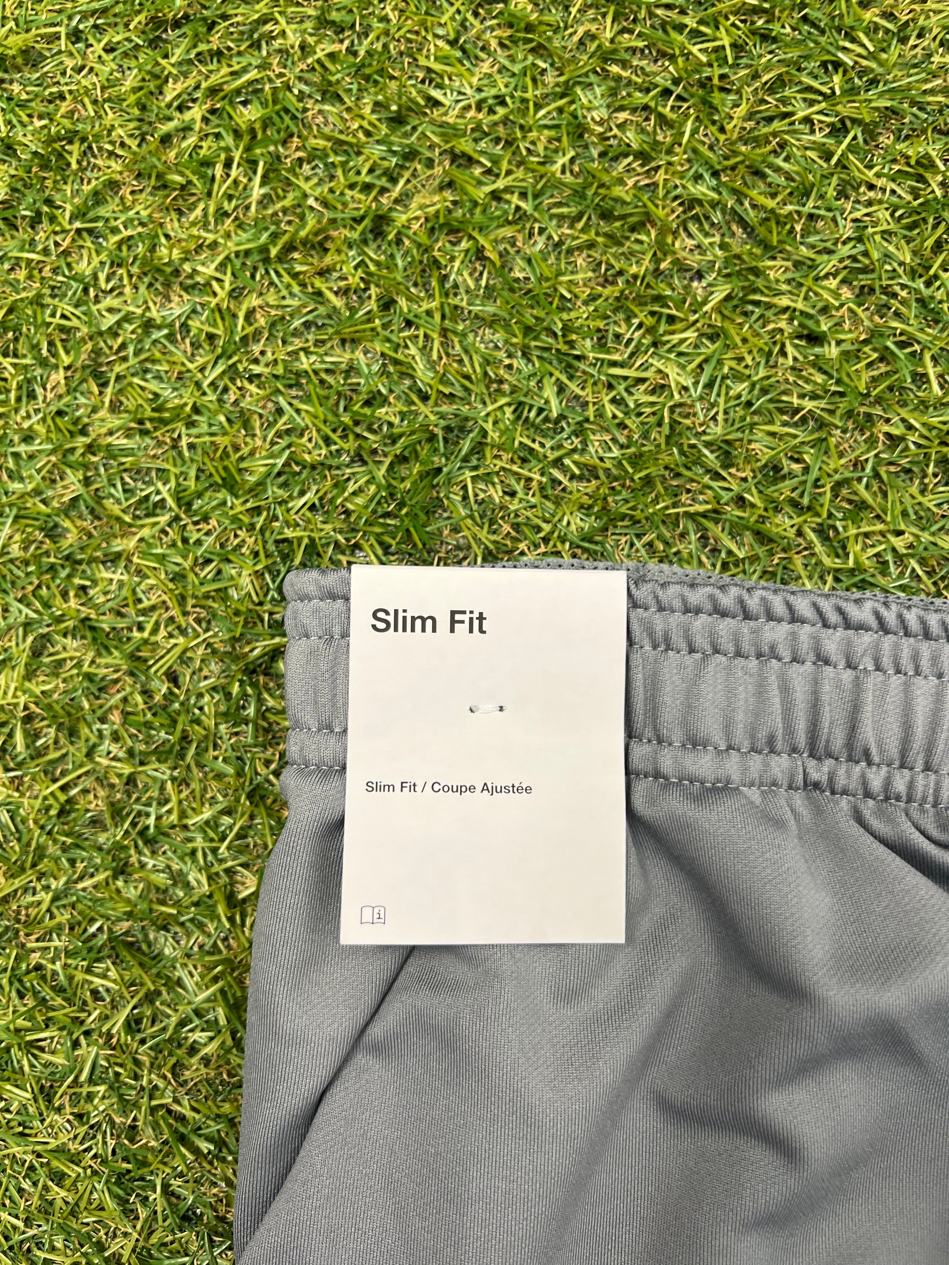 Tag showing 'Slim Fit' label attached to waistband of grey tracksuit bottoms