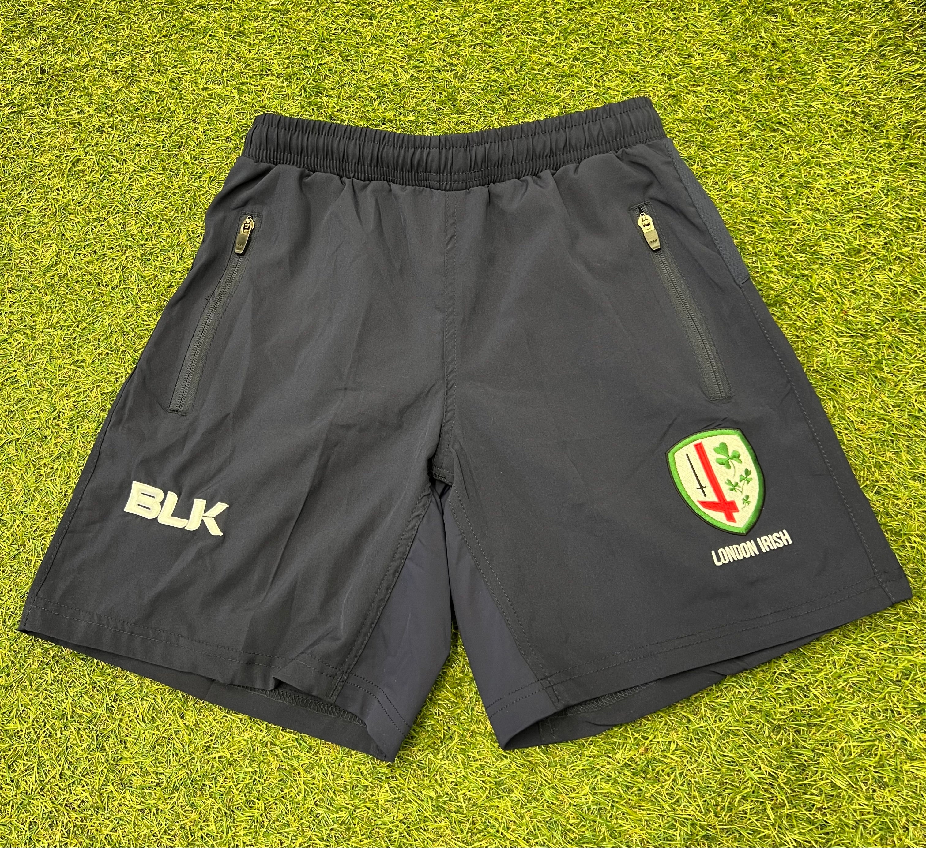 Front view of black BLK London Irish youth sports shorts with zipped pockets and logos.