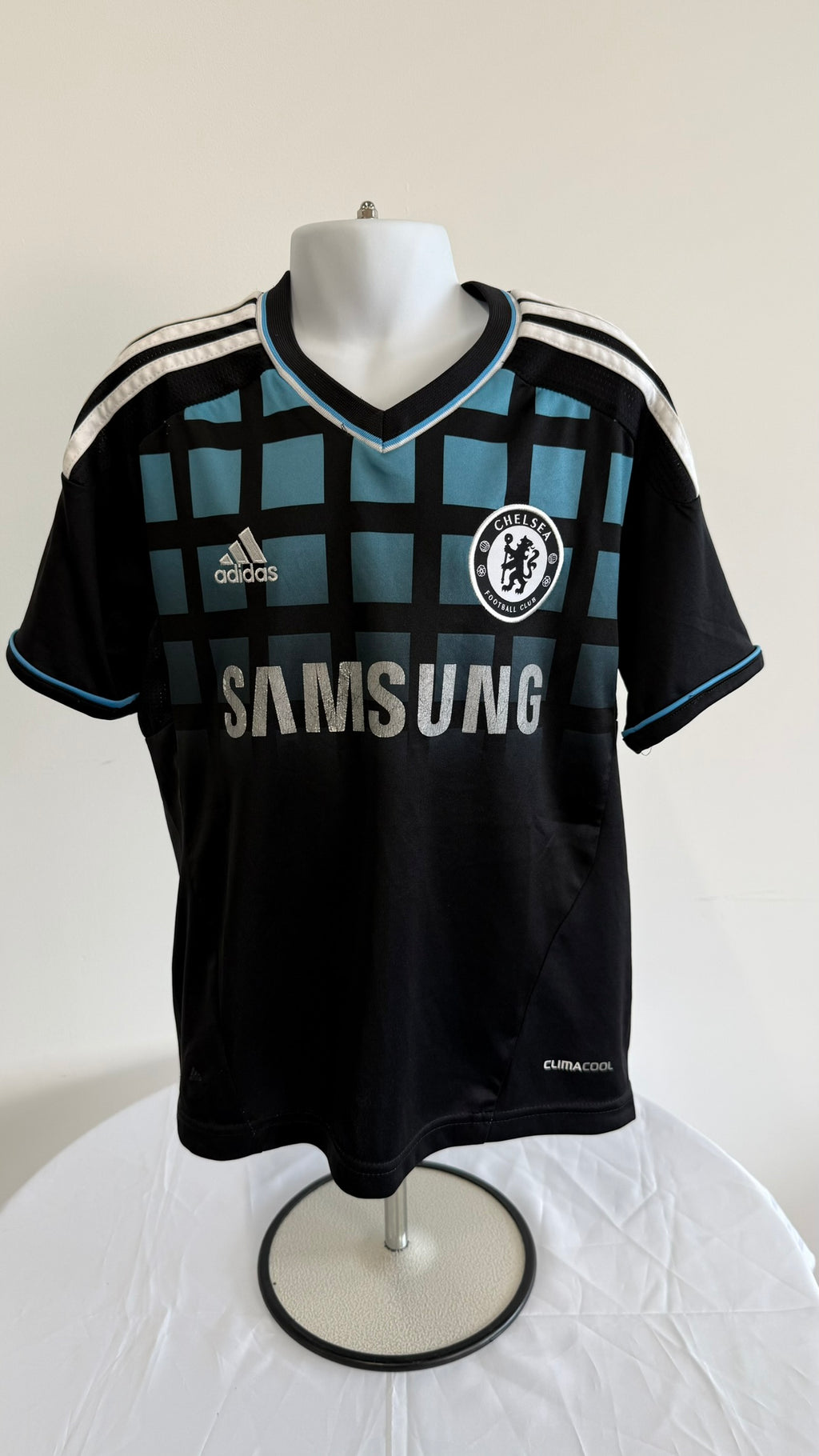 Front view of Adidas Chelsea FC kids' football shirt with black and teal grid design and sponsor logos