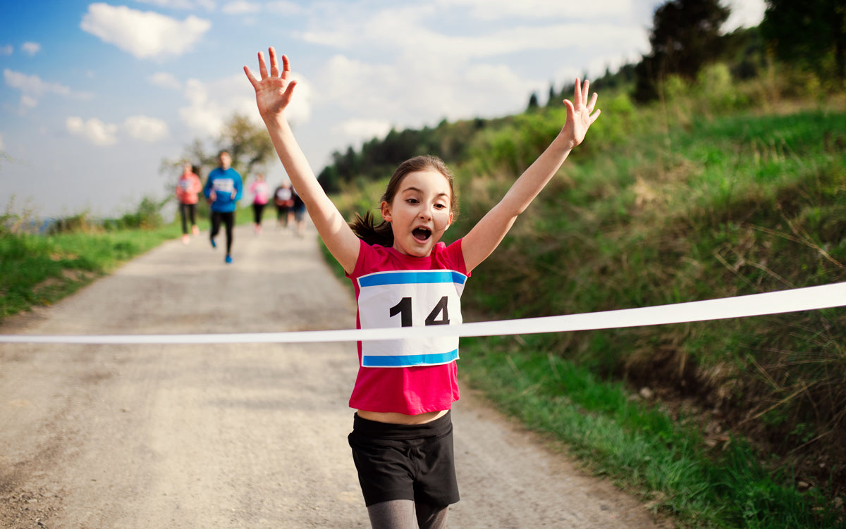 A young girl wins a running race with her hands in the air as she breaks the tape