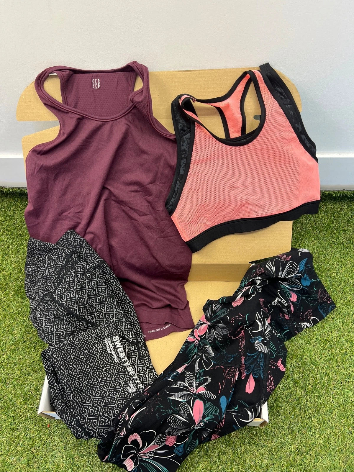 Sweaty Betty gift box with maroon tank top, coral pink sports bra with black trim, and two pairs of patterned leggings, one black and white geometric and one floral design