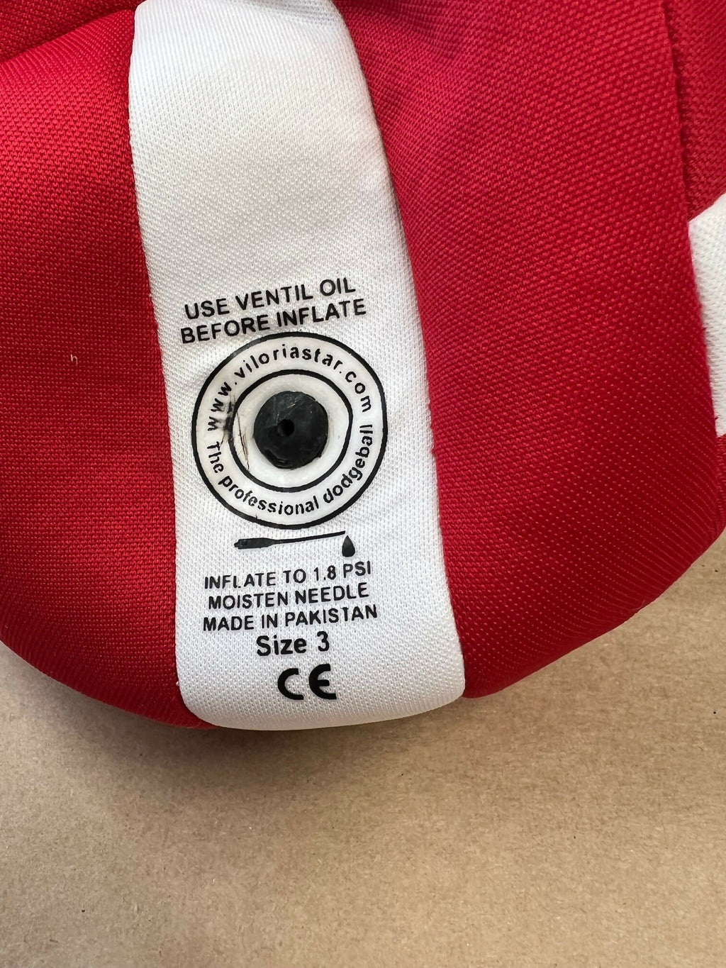 Close-up of inflation valve on red and cream British dodgeball with instructions to use ventil oil before inflating to 1.8 PSI