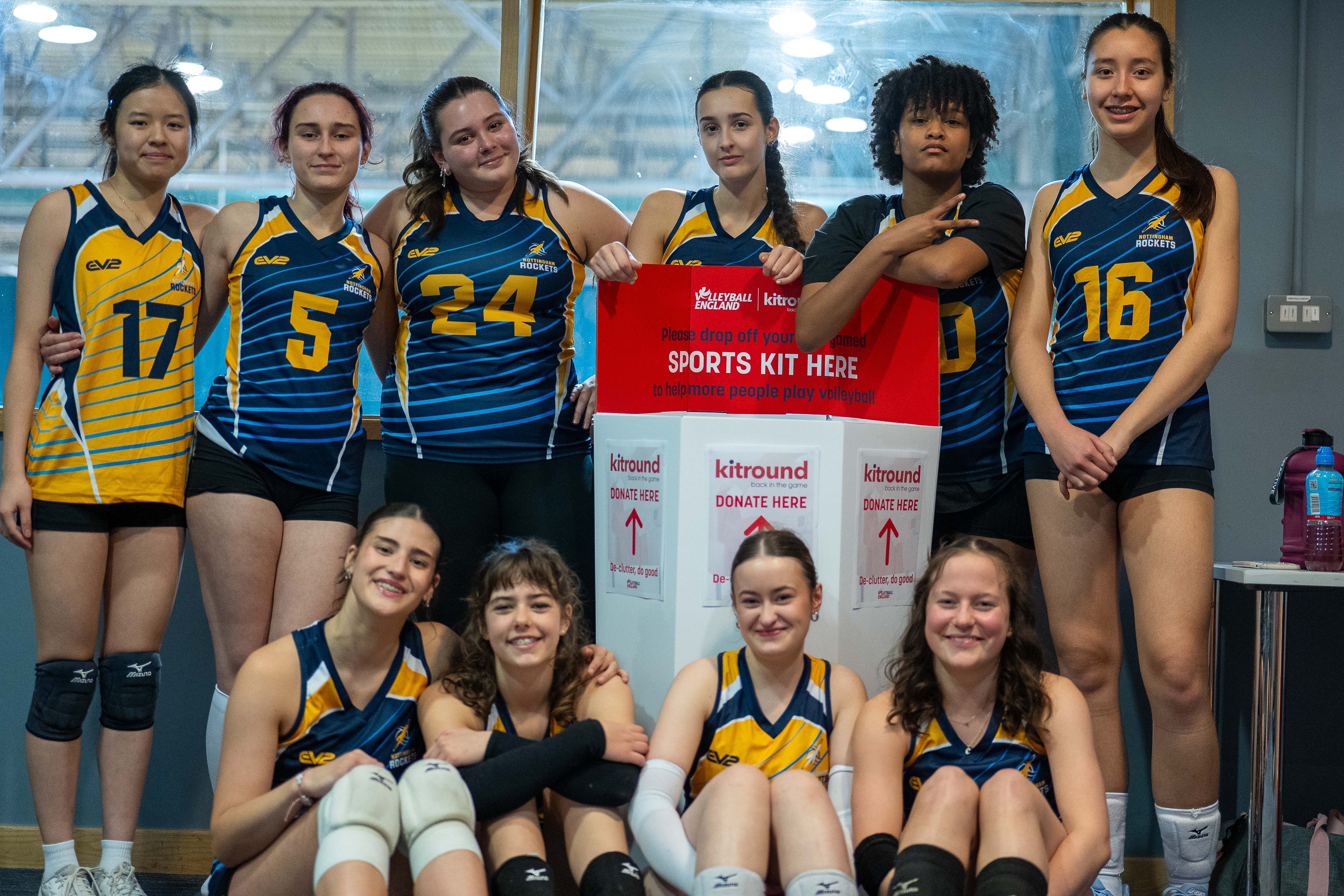 Group of young women in sports uniforms posing with a kitbin collection box
