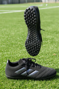 Pair of black adidas astro turf football boots on artificial grass with studded rubber sole visible
