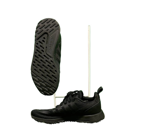 Pair of black adidas Multix trainers on display with green background and one shoe showing the sole