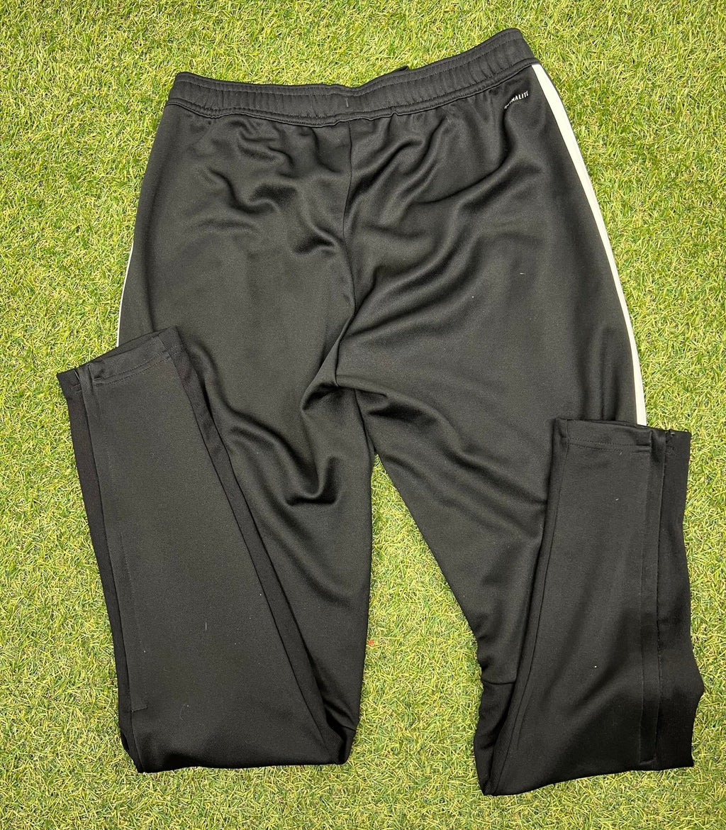 Back view of black adidas tracksuit bottoms with striped sides, laid on grass