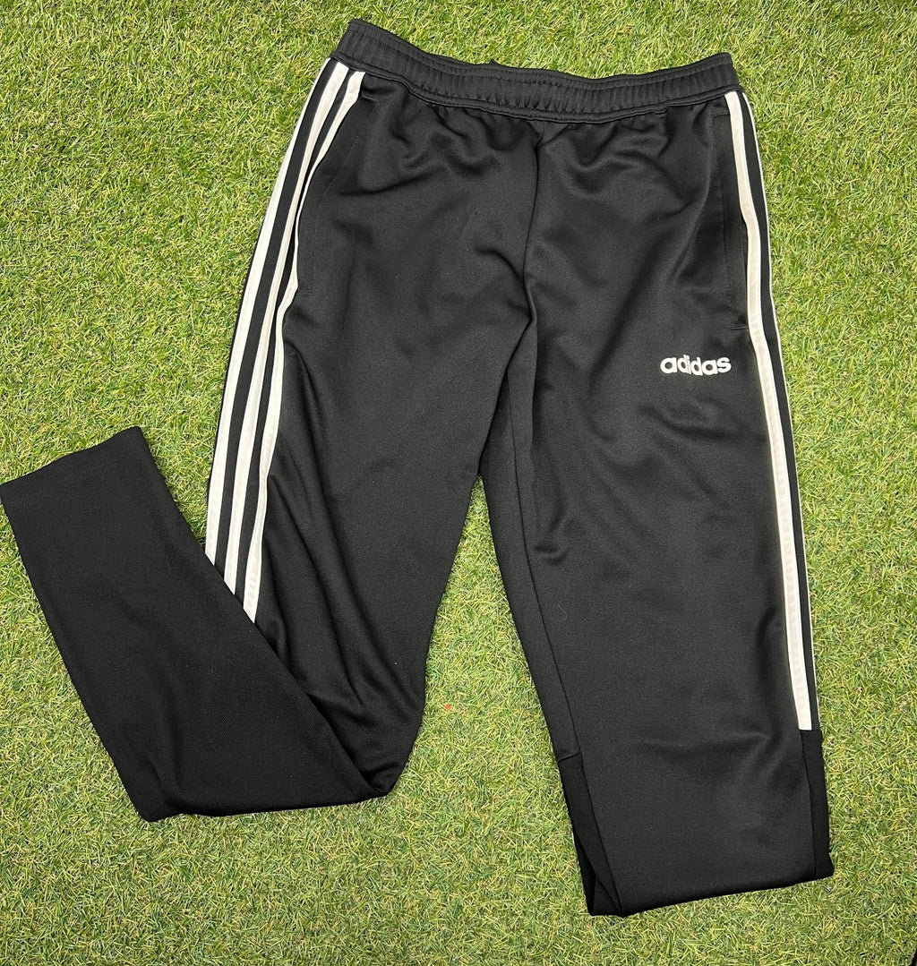 Black adidas tracksuit bottoms with three white stripes, laid flat on grass
