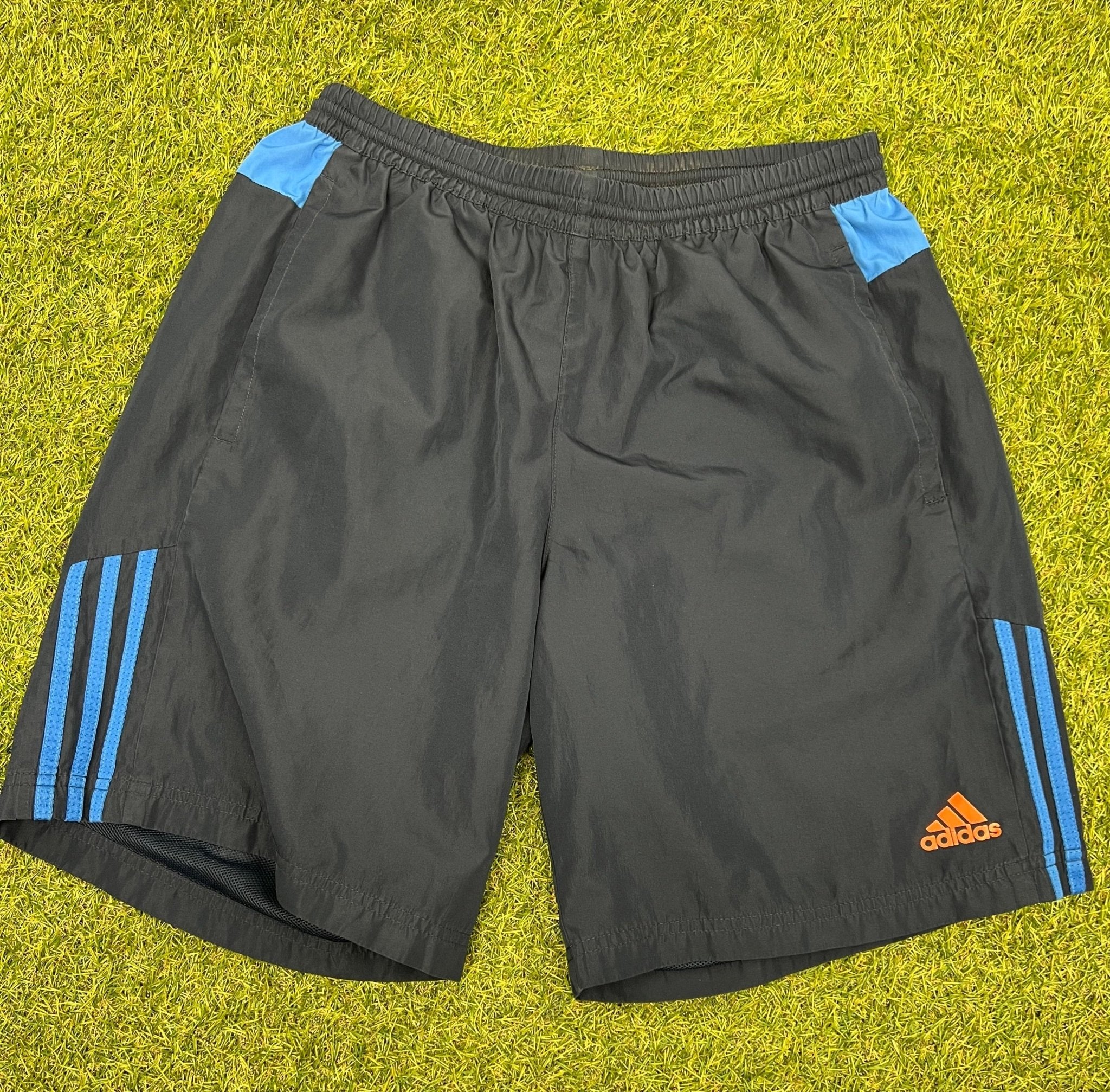 Front view of dark blue adidas sports shorts with blue stripes and orange logo