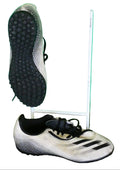 Pair of white and black adidas turf football boots with a textured sole displayed on artificial grass