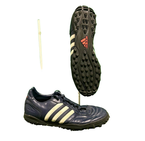 Pair of navy Adidas football boots with white stripes and rubber studded soles on artificial grass