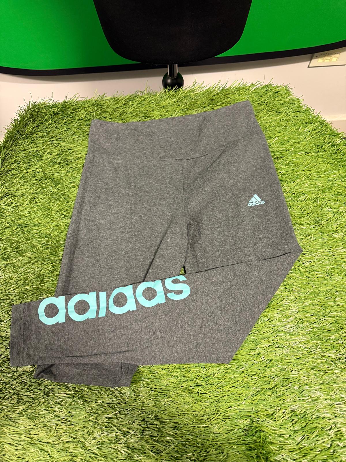 Grey Adidas leggings with blue logo and branding, displayed on green surface