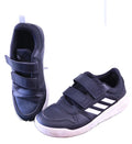 Top view of black Adidas trainers with white stripes and Velcro fastenings shown on artificial grass