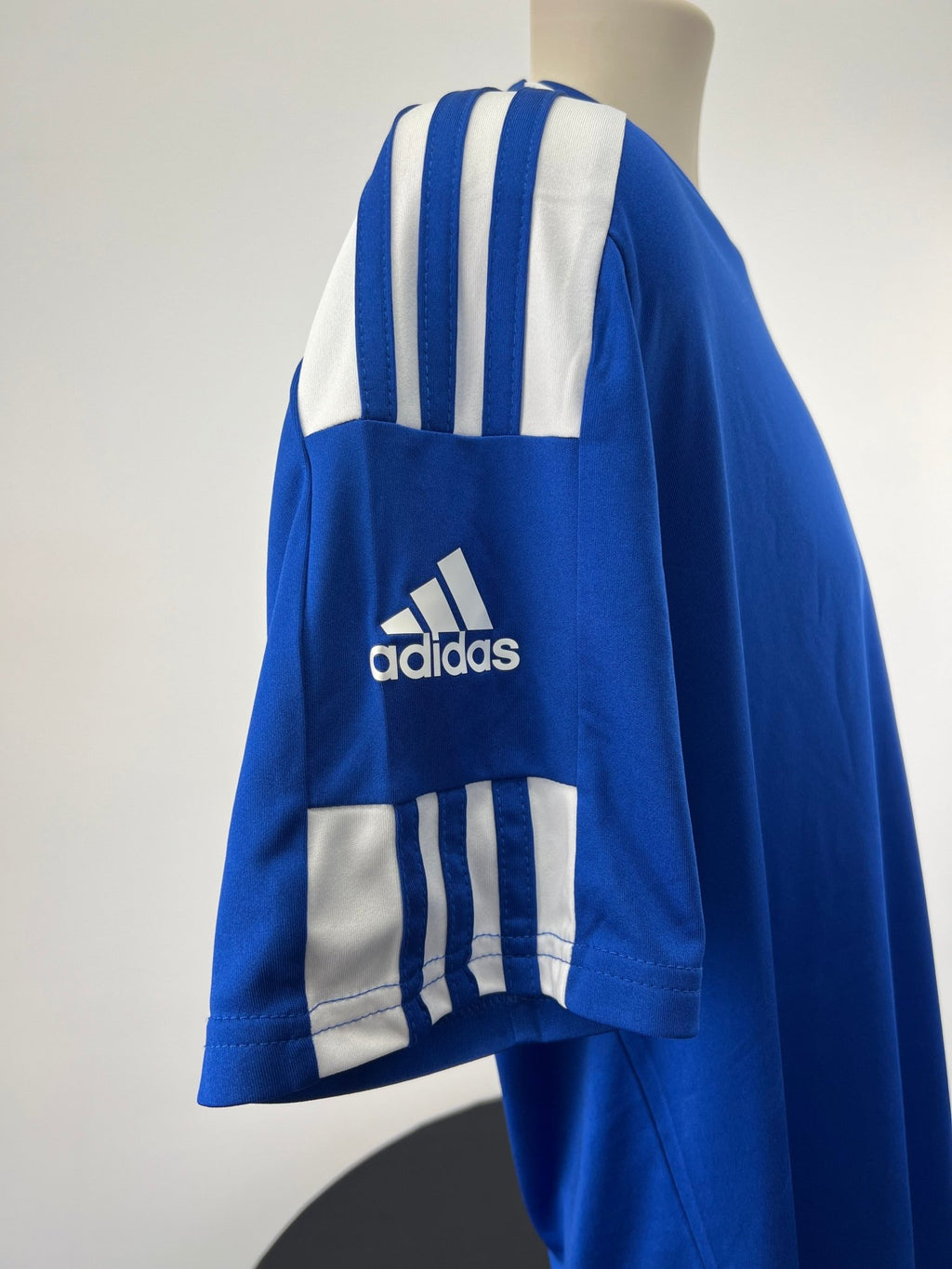 Side detail showing adidas logo and sleeve stripes on blue T-shirt.