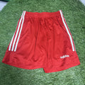 Red Adidas football shorts with white side stripes laid on artificial grass