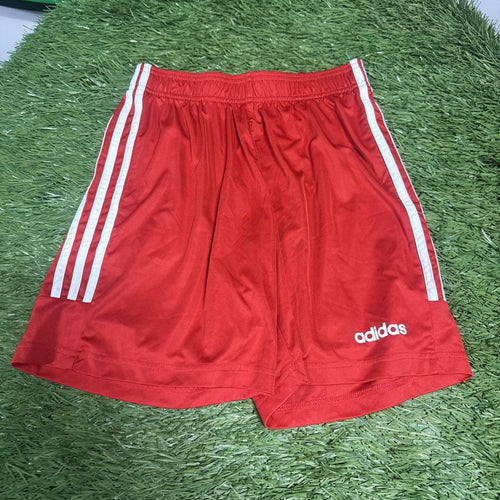 Red Adidas football shorts with white side stripes laid on artificial grass
