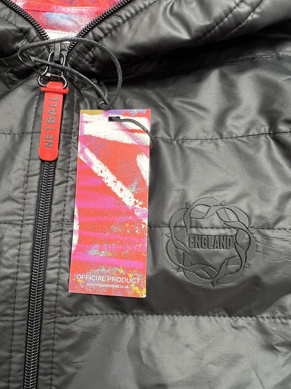 Close-up of England Netball badge and official product tag on black quilted jacket