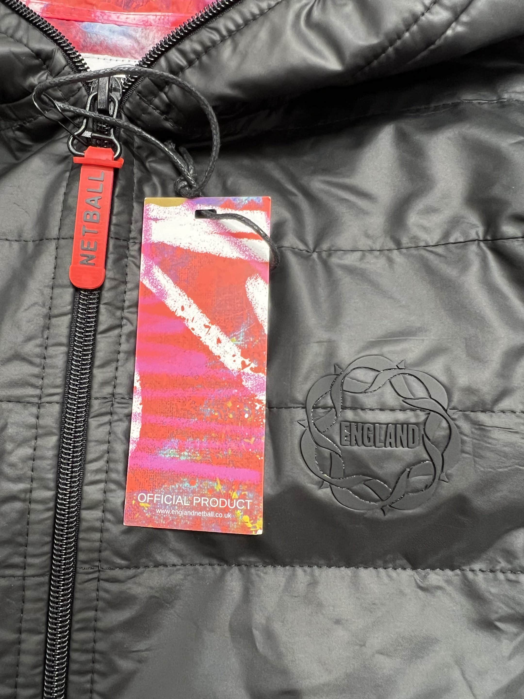 Close-up of England Netball badge and official product tag on black quilted jacket