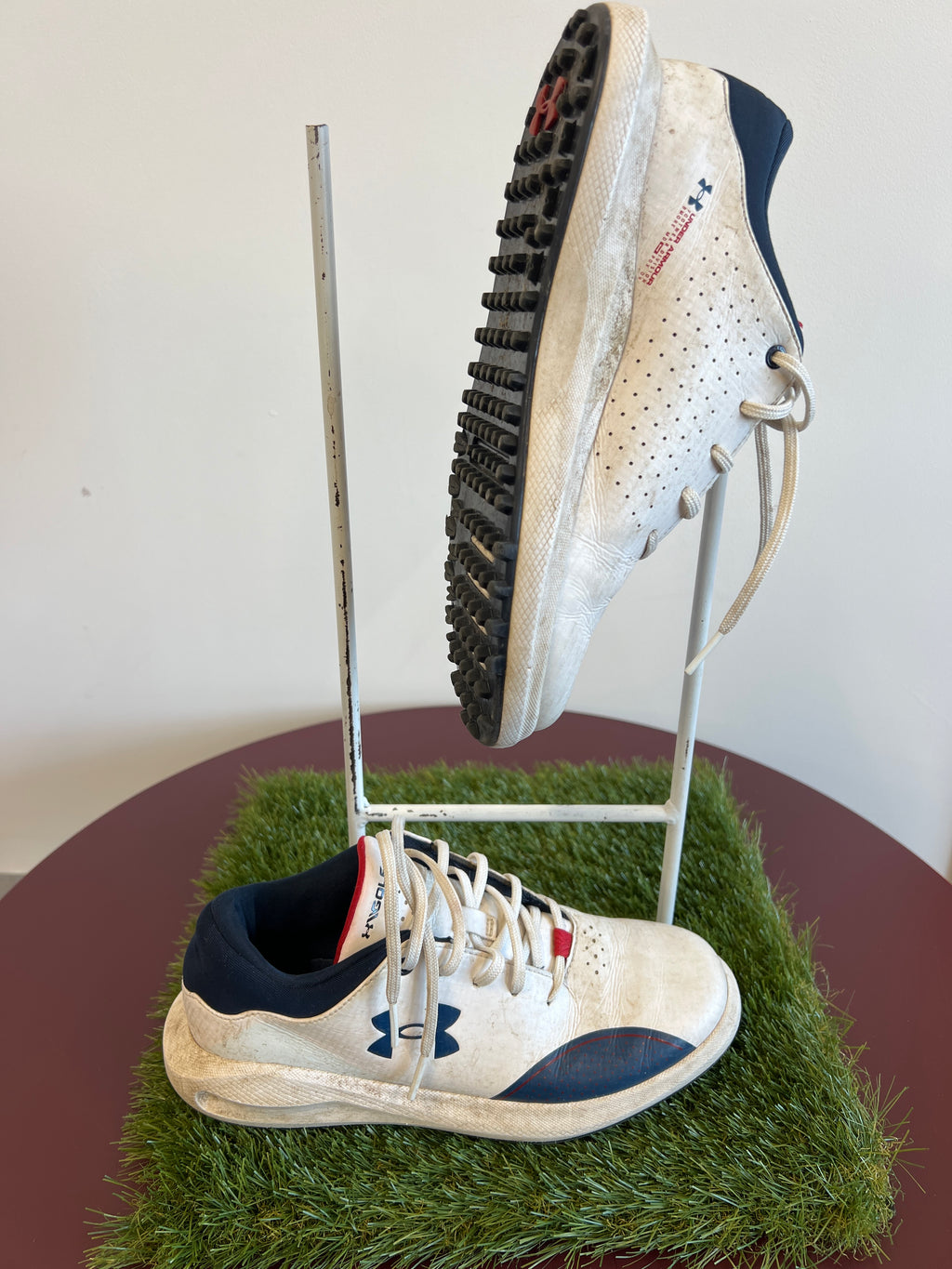 Side and sole view of Kids Under Armour golf shoe showing black studded outsole and logo