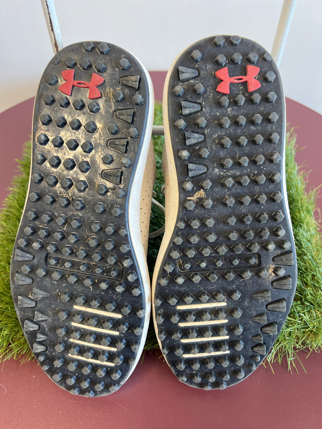 Bottom view of black studded outsole of Kids Under Armour golf shoes with red logos
