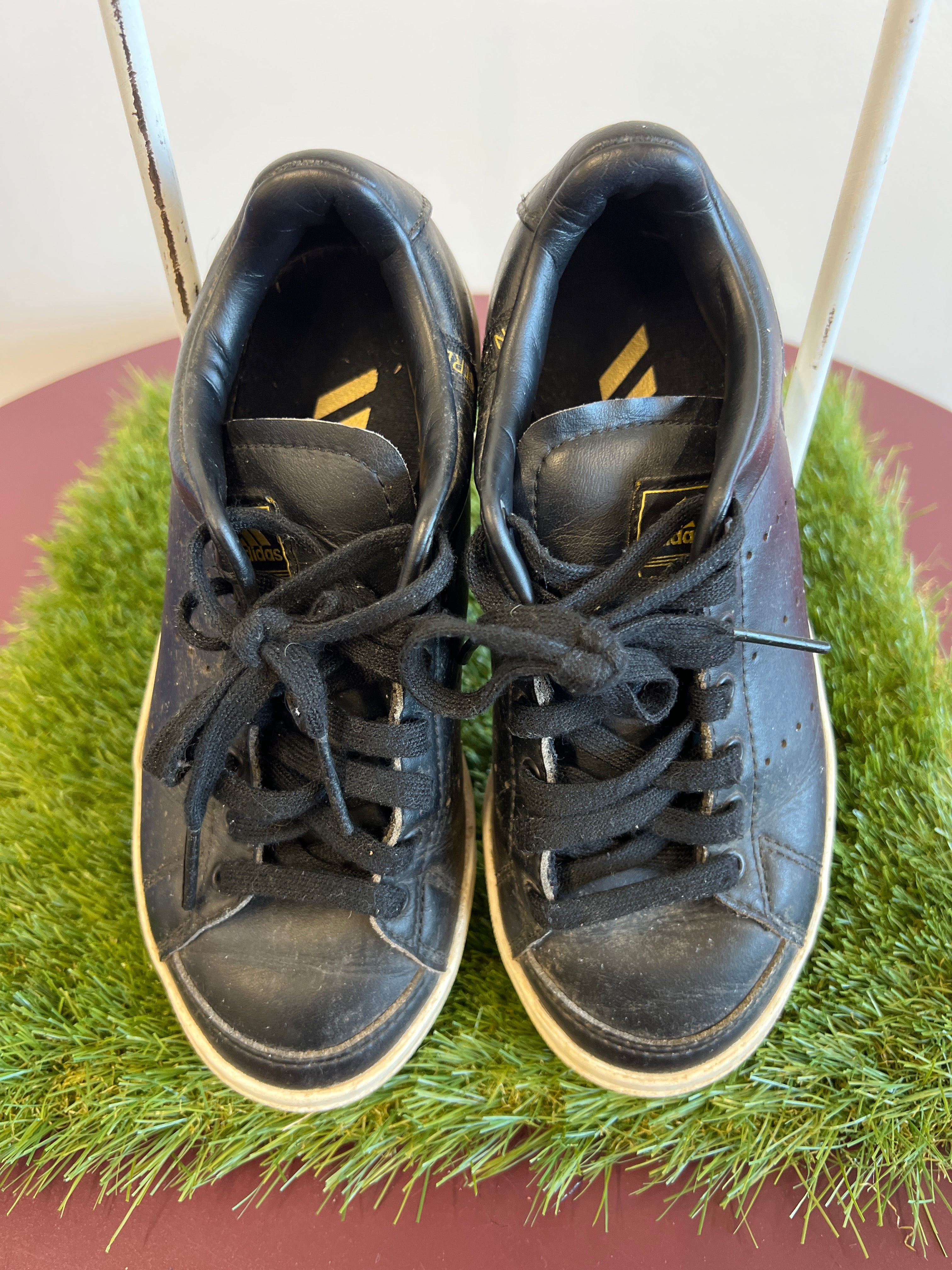 Top view of black kids adidas Astro Boots with laced uppers on green grass mat