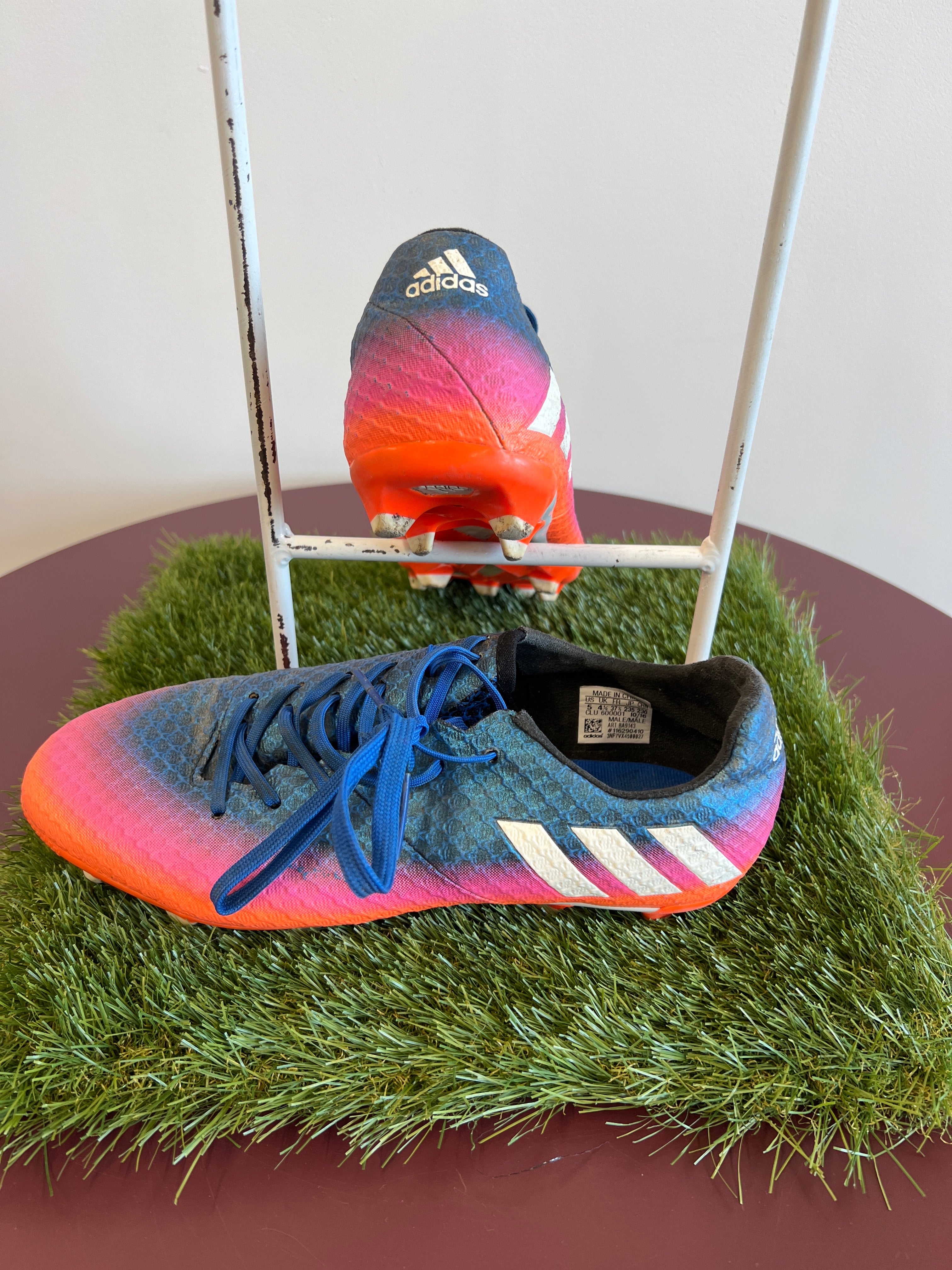 Side and rear view of kids adidas football boots showing three white stripes and molded studs on artificial grass