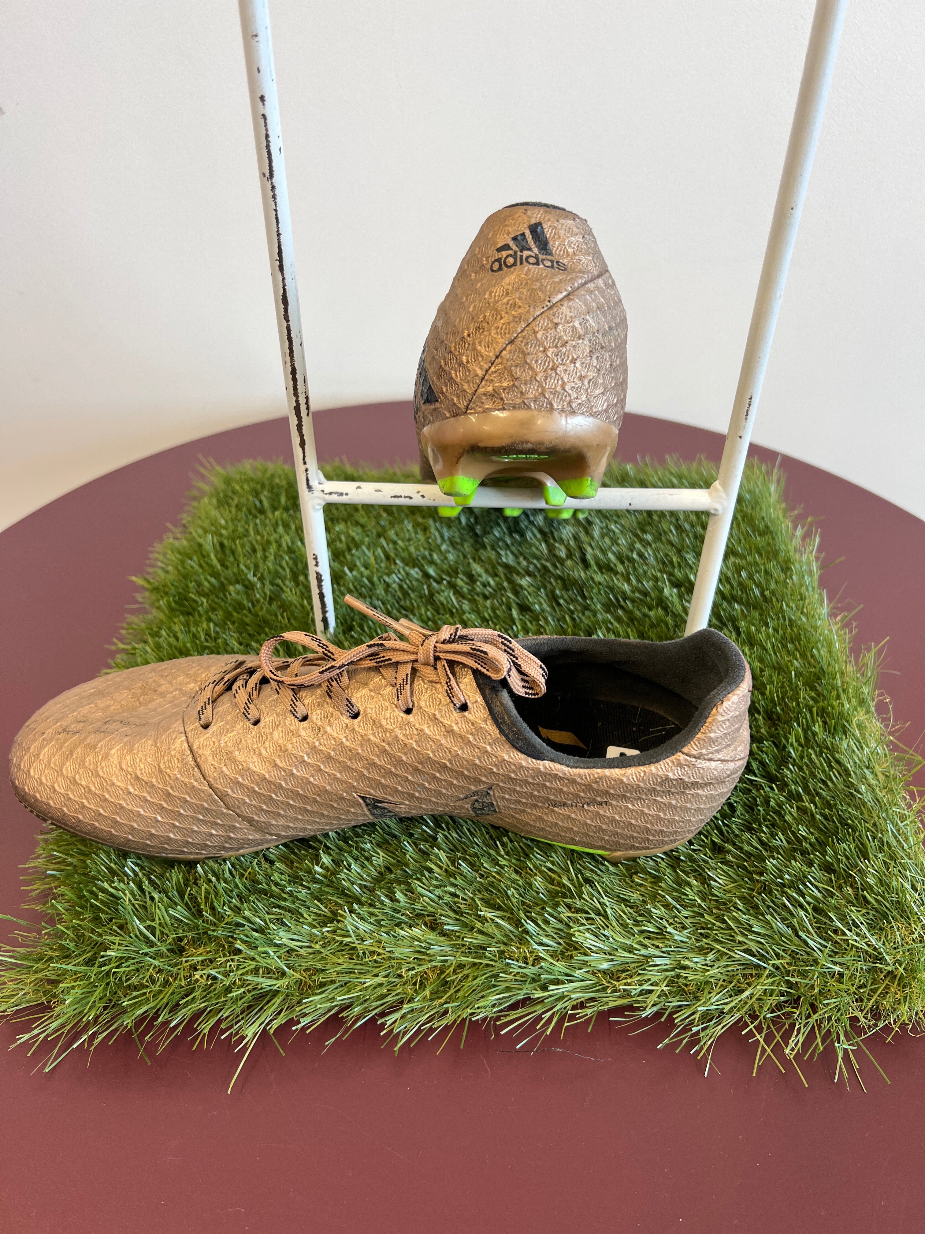 Side and rear view of kids adidas football boot displaying black adidas logo on gold fabric with studded heel