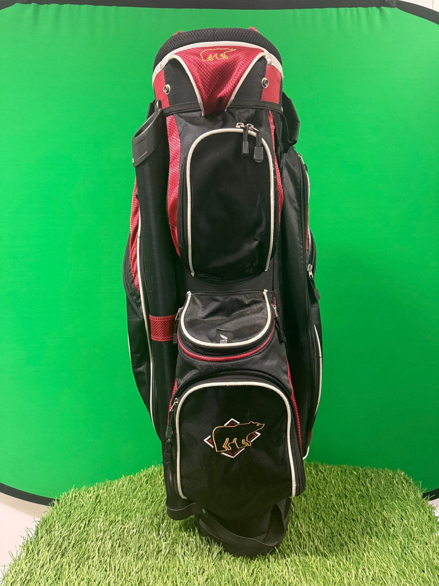 Front view of a Jack Nicklaus Golden Bear golf cart bag in blue-dark with red accents and embroidered bear logo, shown standing on artificial grass.